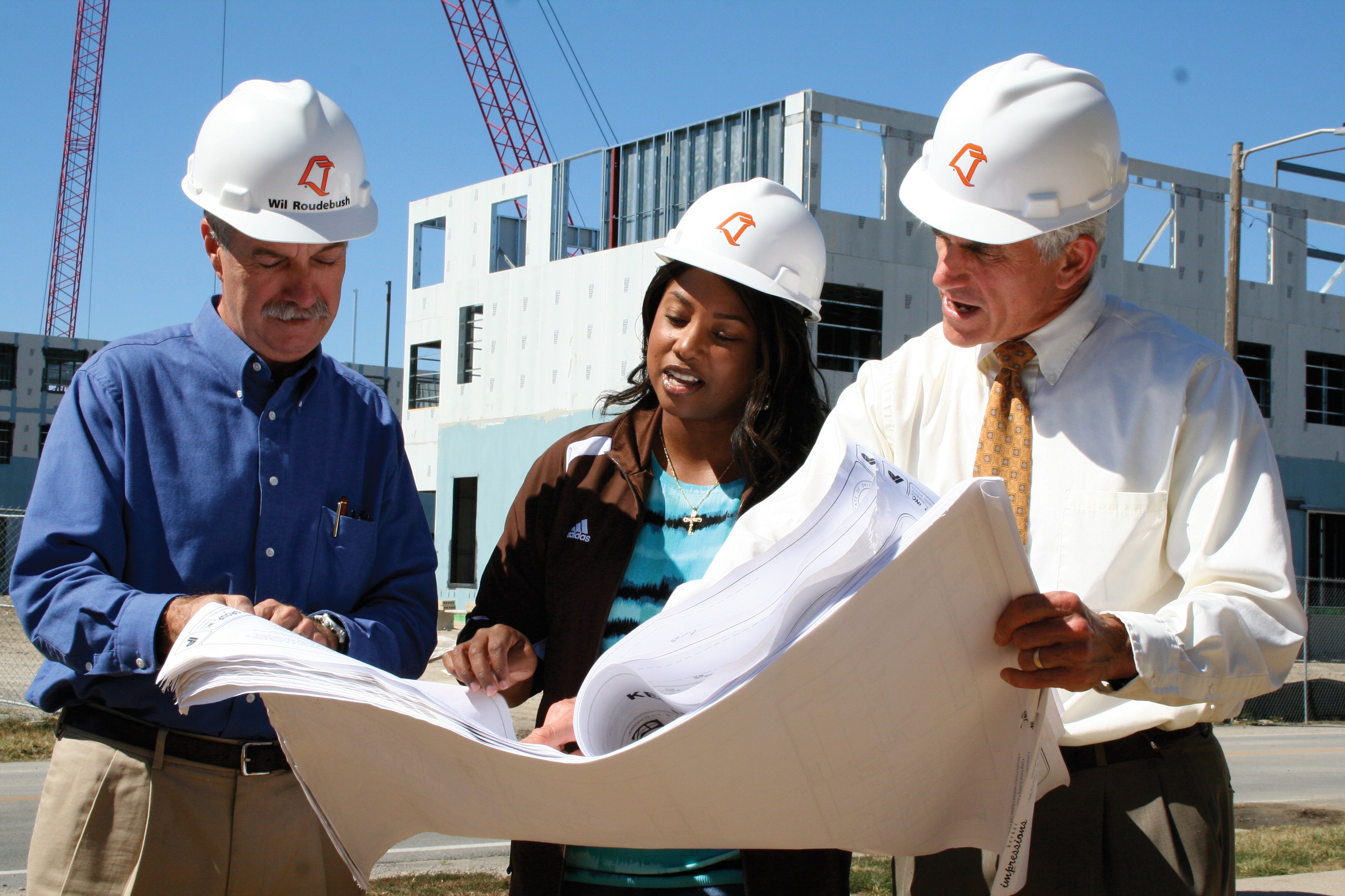 Construction Management and Technology students on a construction site looking at blueprints discussing career options with a Masters.