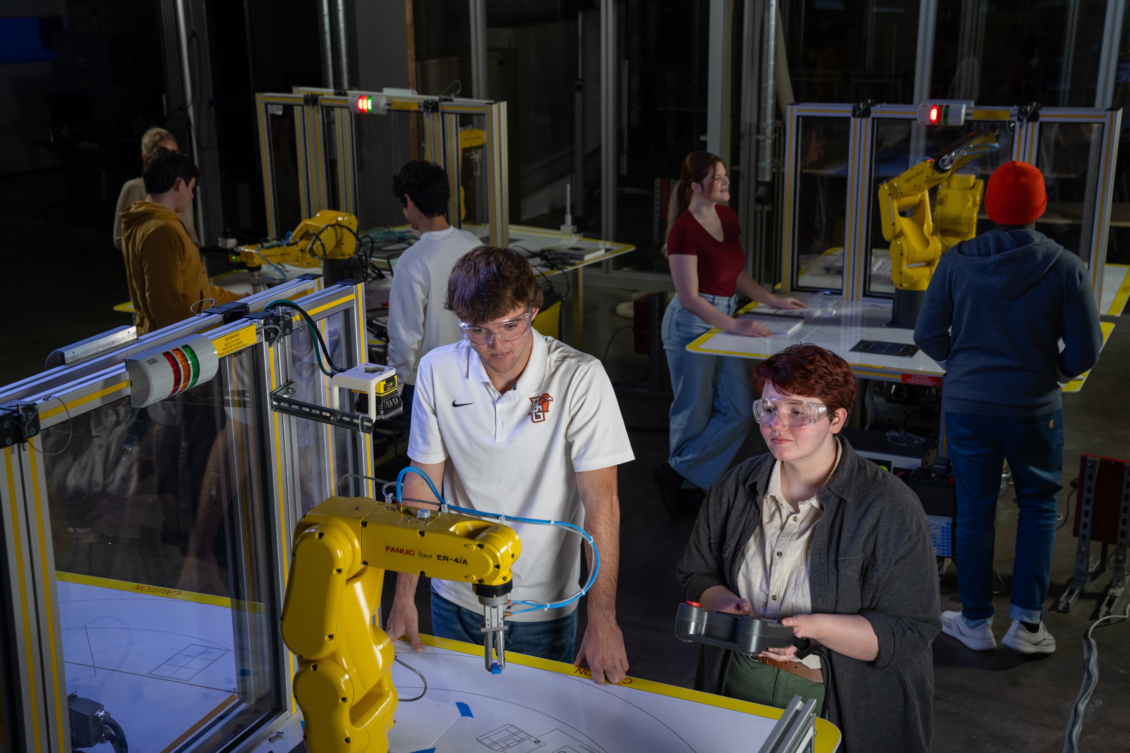 Students work on yellow manufacturing robots in a lab.