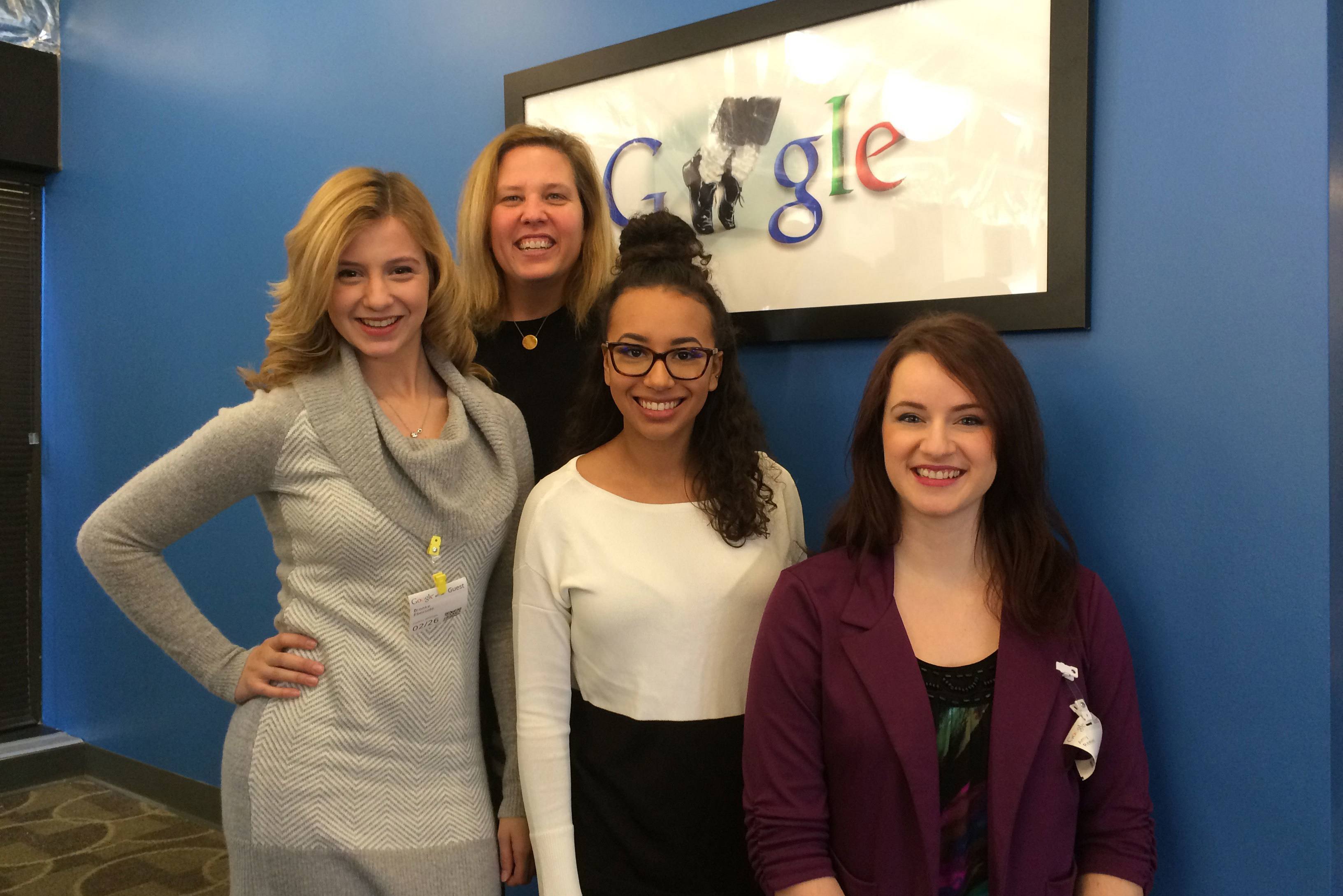 3 public relations students stand with a professor in front a picture of the Google logo