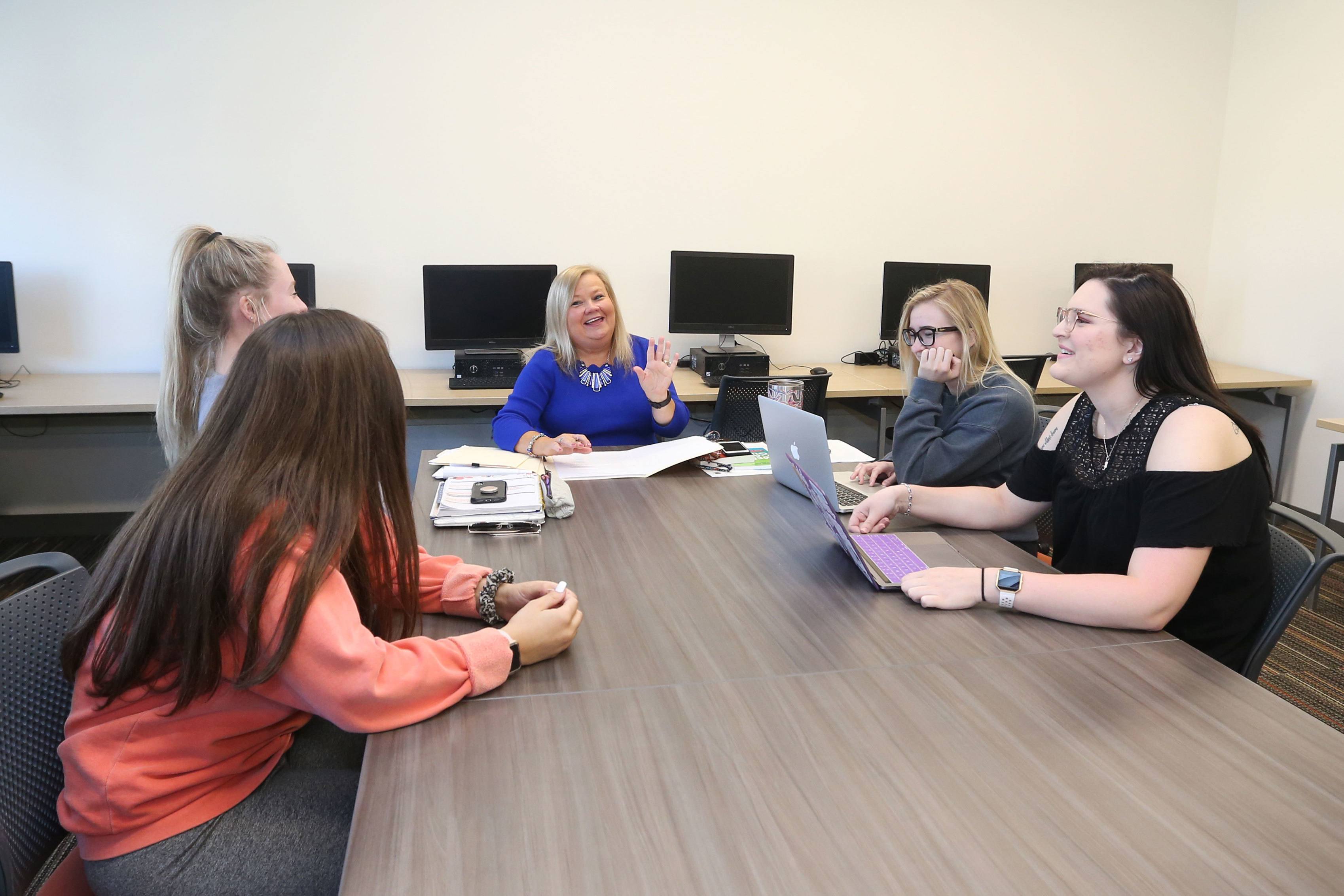 A public relations professor is sitting and talking with a group of students. 