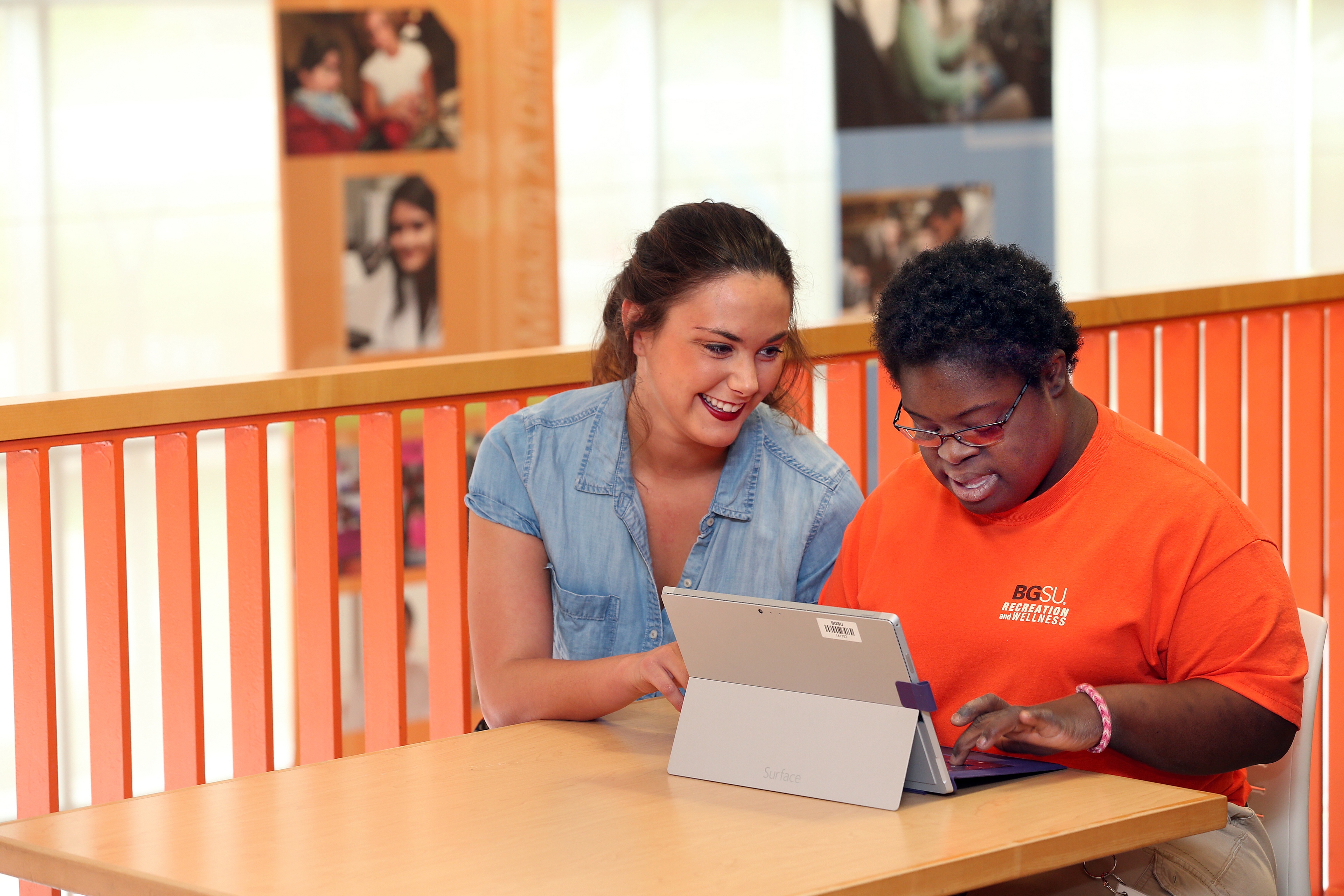 A female assistive technology master’s student helps a young woman with disabilities use a computer.