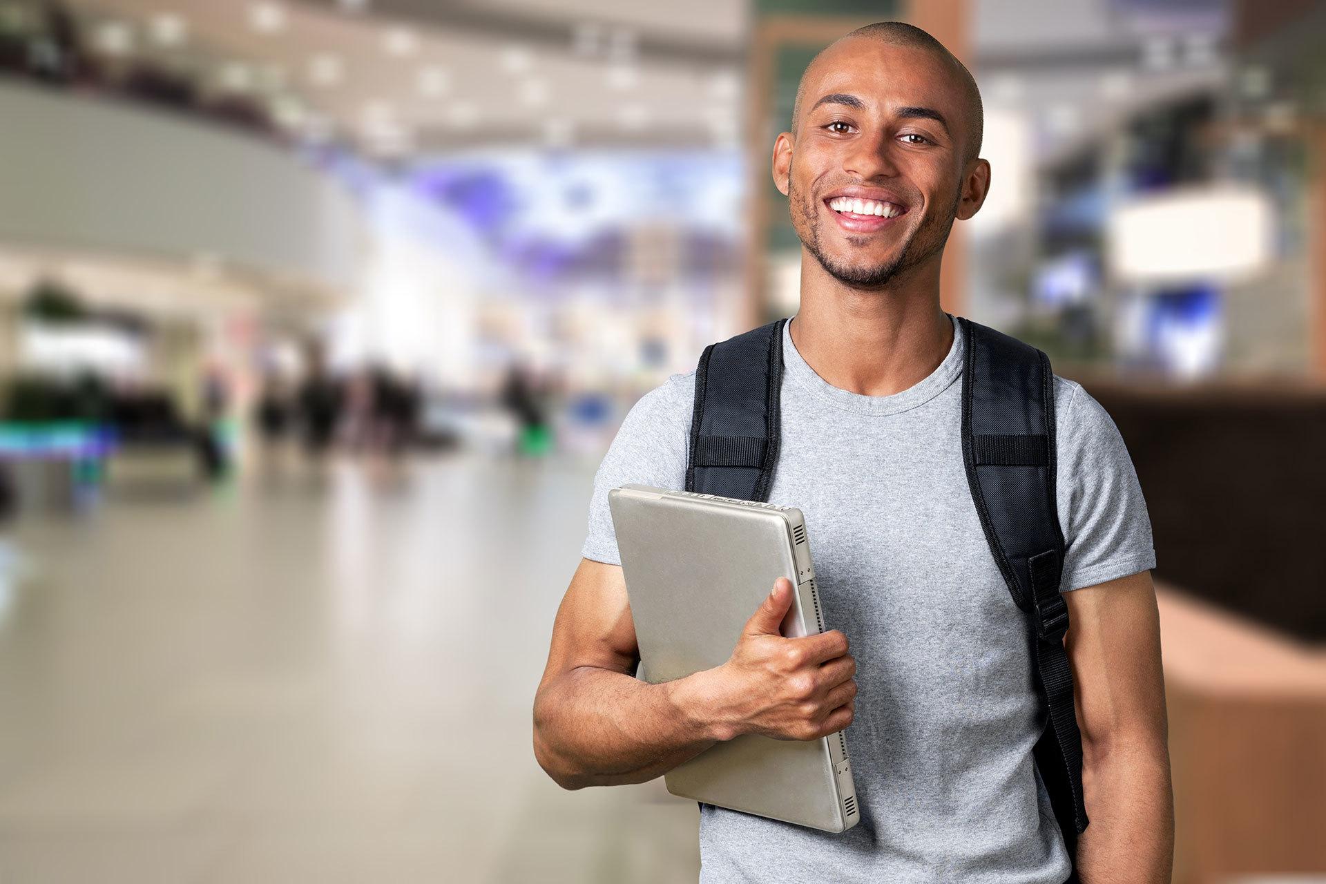 student in a gray t-shirt, holding a binder and smiling