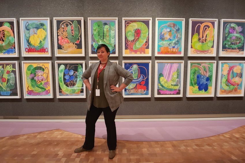 Alumni Duffee Maddox posing in front of a gallery of hanging artwork