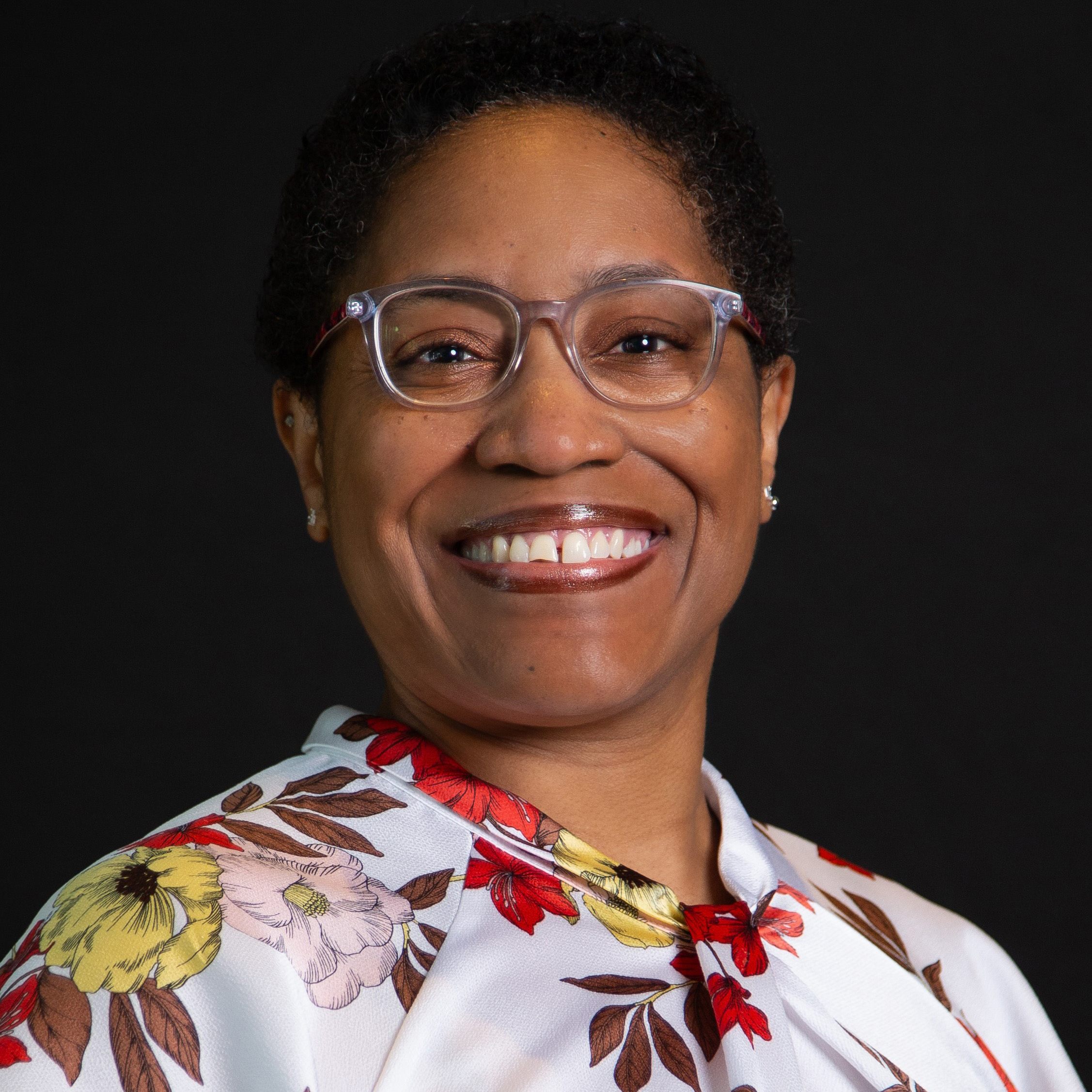 Headshot of woman of color with short hair wearing glasses and a floral blouse