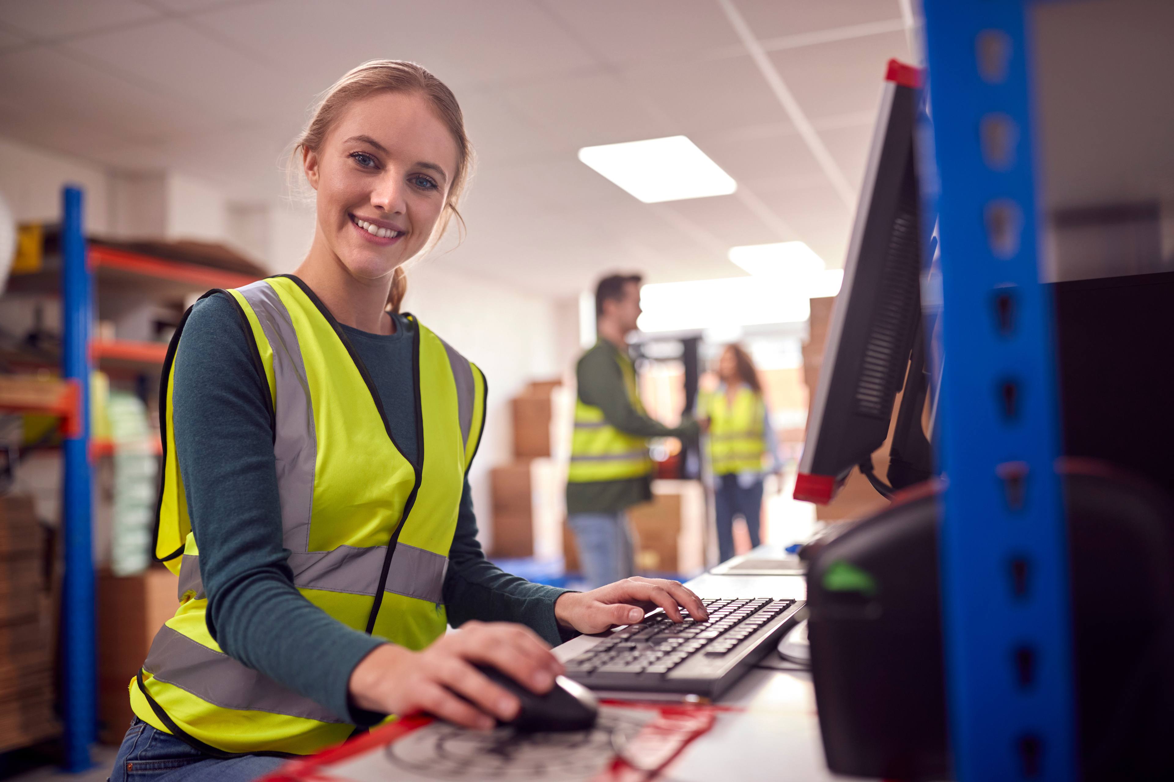 Portrait Of Female Worker In Busy Modern Warehouse Working On Computer Terminal