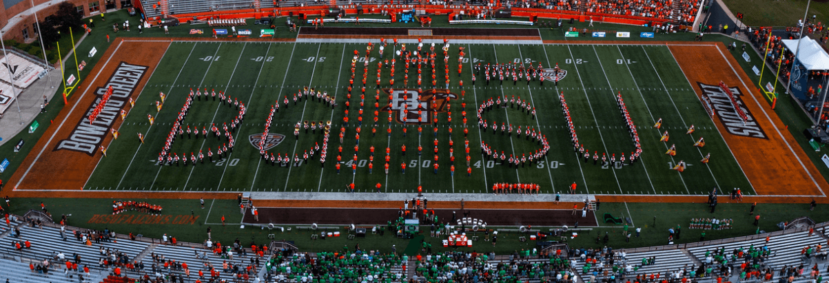 BGSU Falcon Marching Band members spell out B G S U with nine rows of alumni band members standing between the BG and the SU at Doyt Perry Stadium.