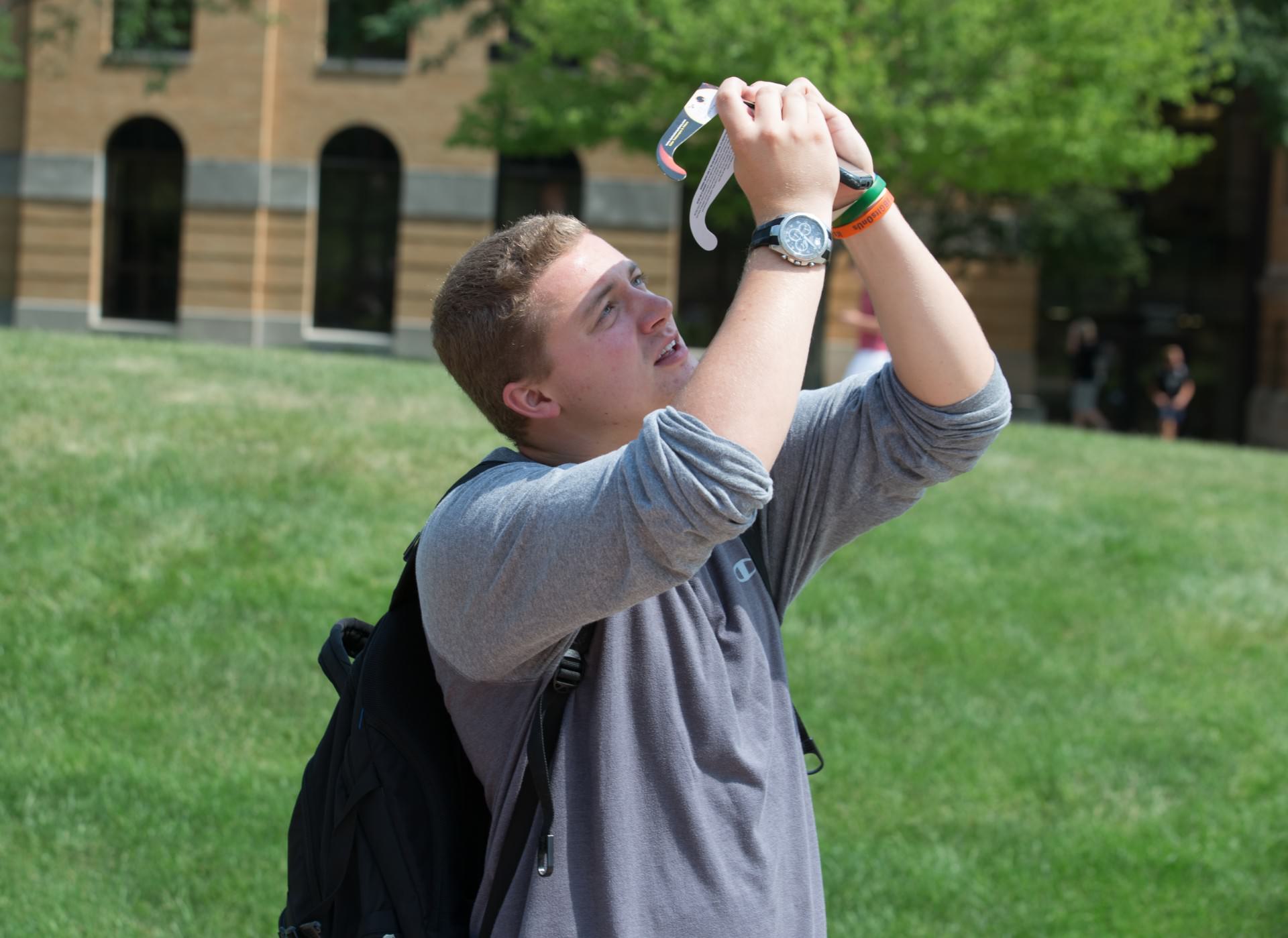 Male student holding solar eclipse glasses over his phone camera