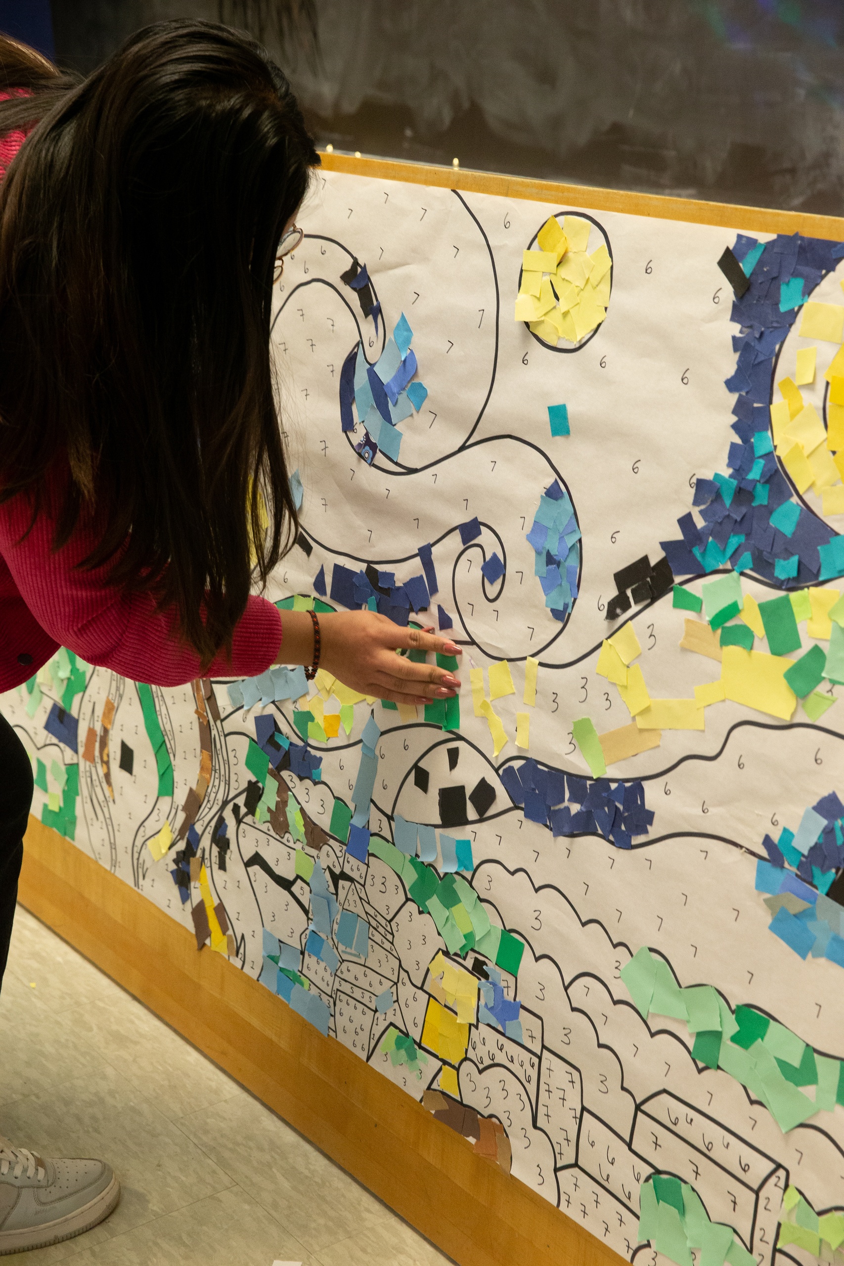 An individual places a piece of colored paper on the a large, community color by number display