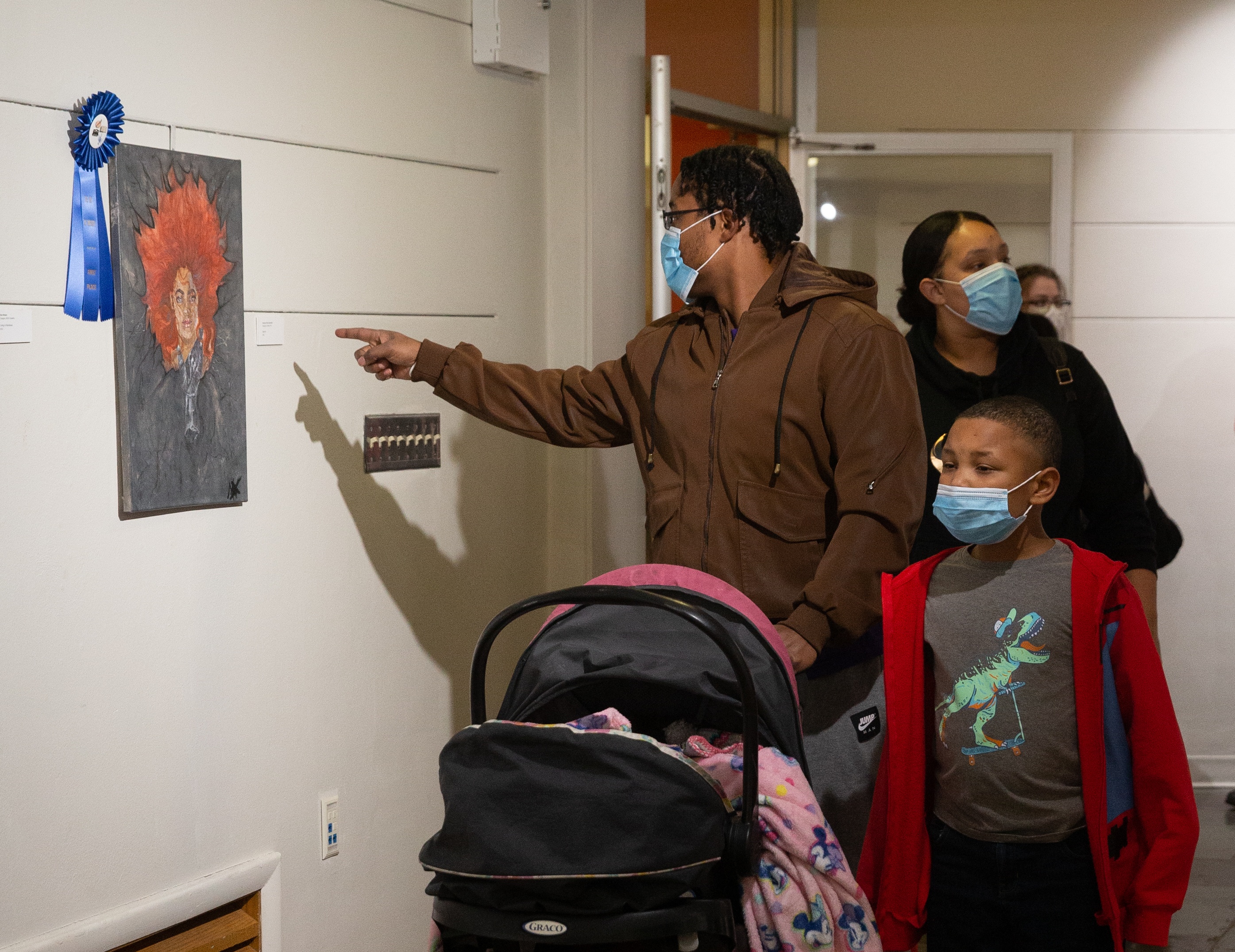 A family walking as the man is pointing at an Art of Diversity painting