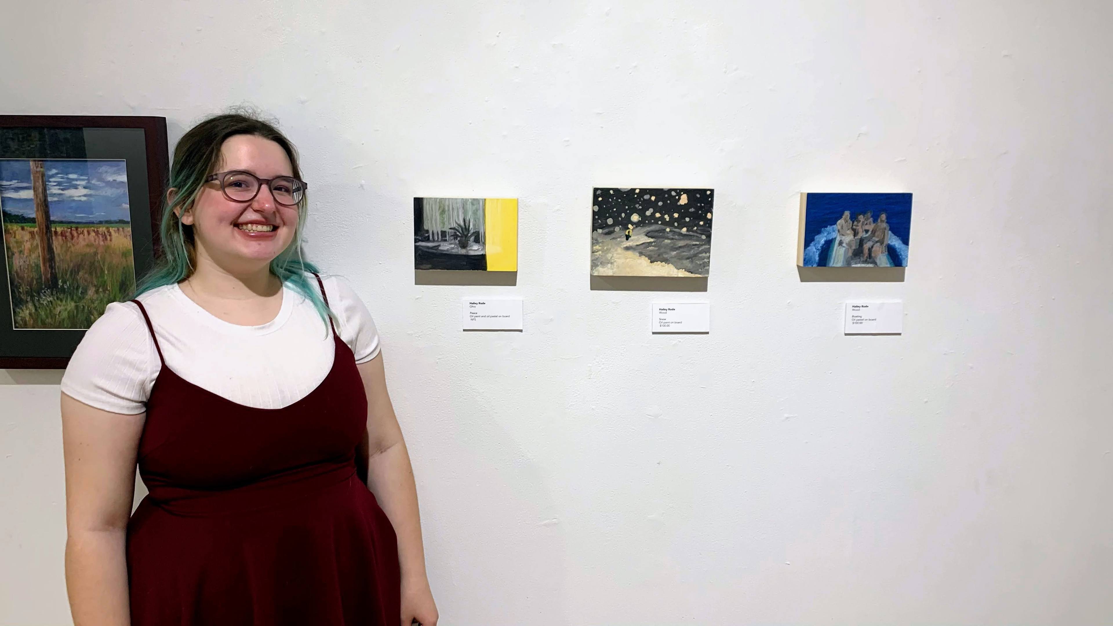 BGSU senior Hailey Rode smiling in front of her several paintings