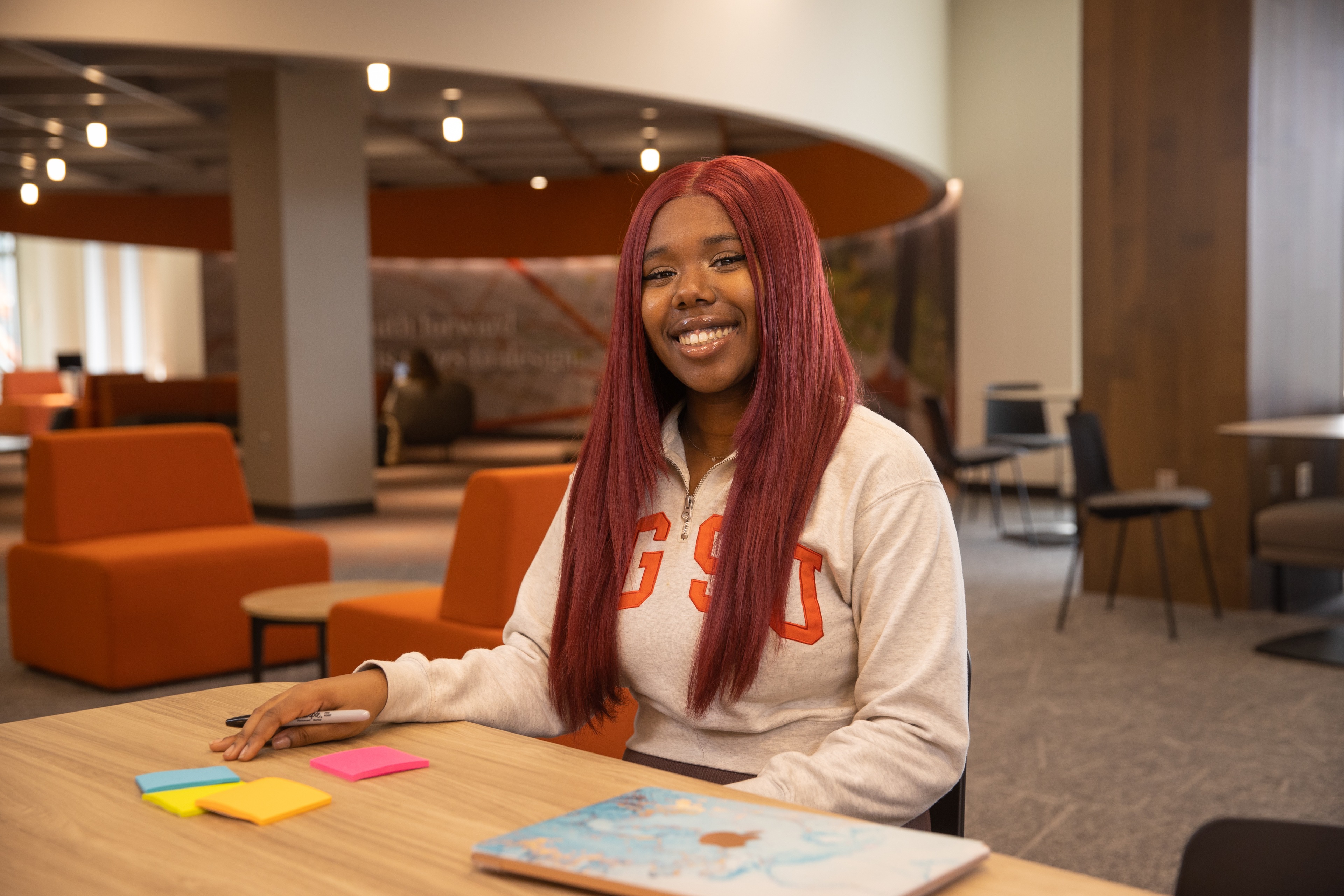 Student Briyanna sits at a table with sticky notes and her laptop. She is wearing a BGSU sweatshirt