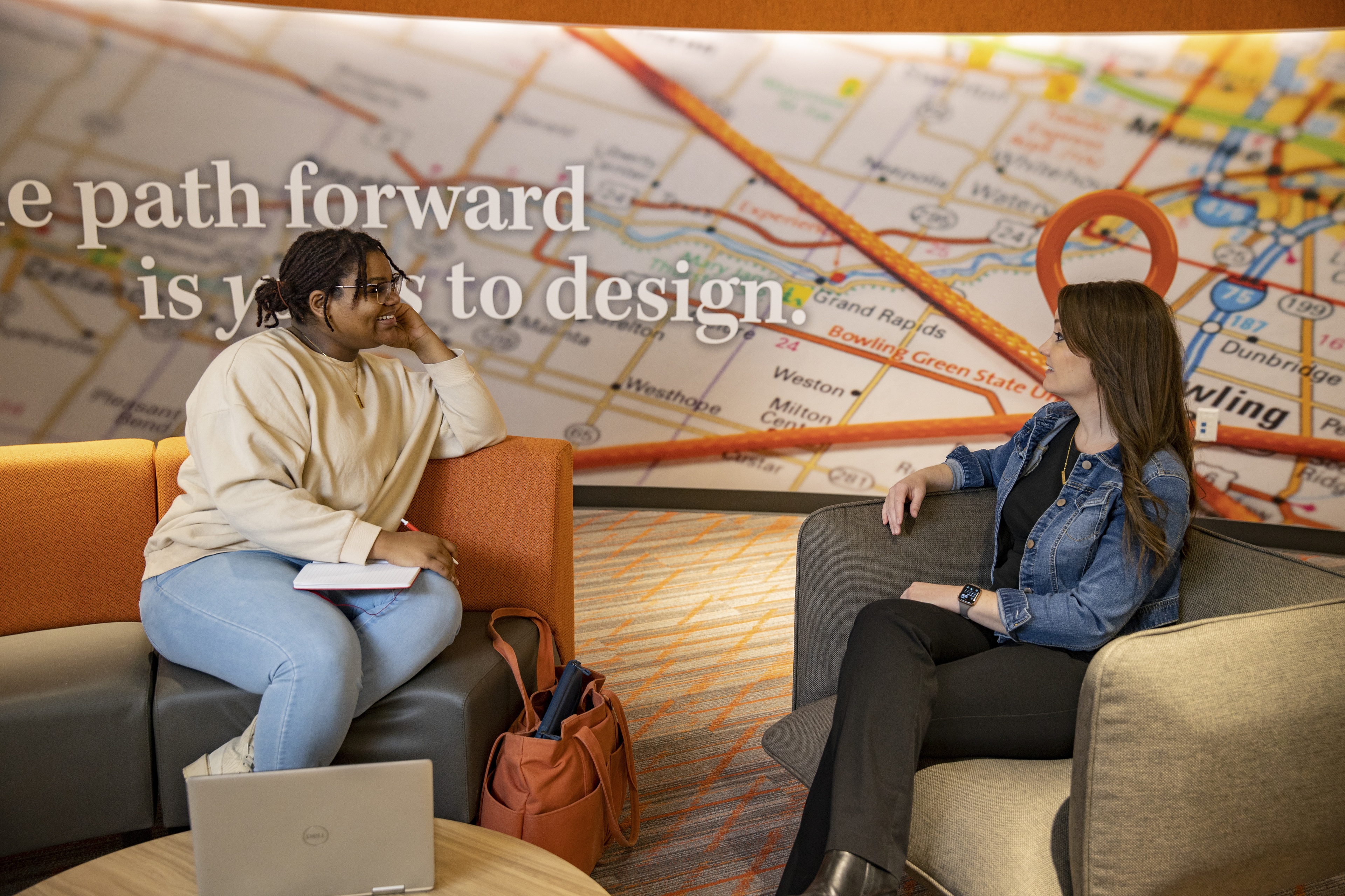 Two women sit across each other in arm chairs. They are smiling and interested in what each other is saying.