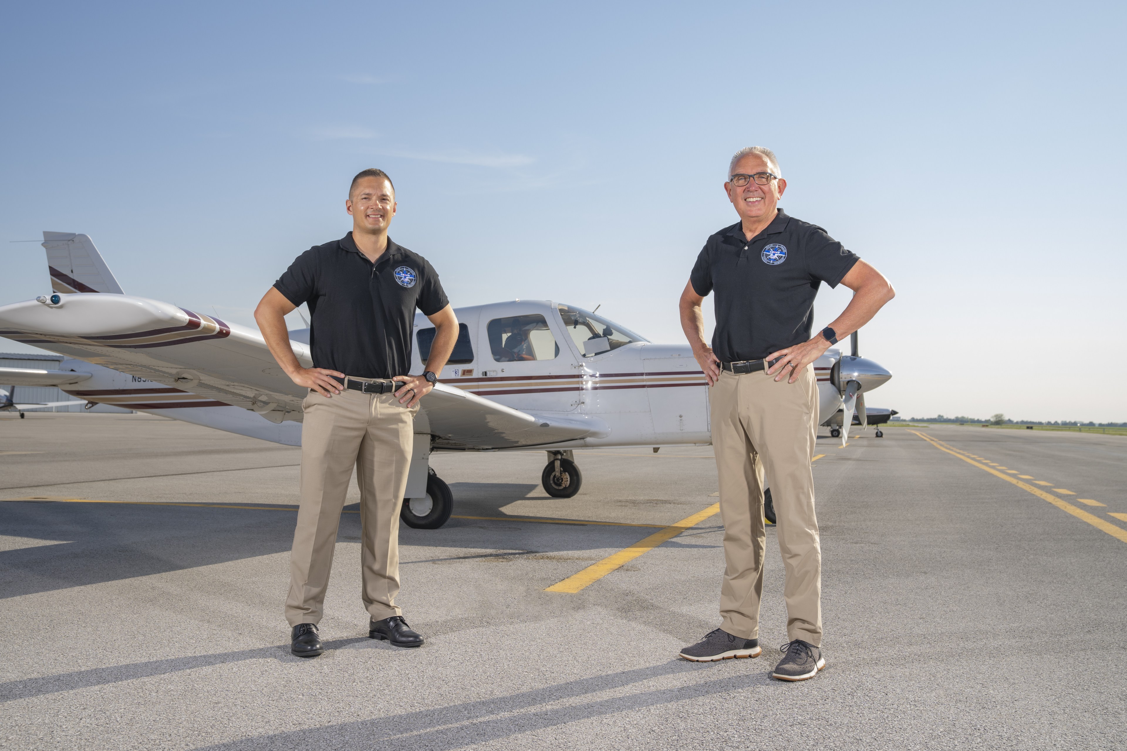 Two men pose next to an airplane