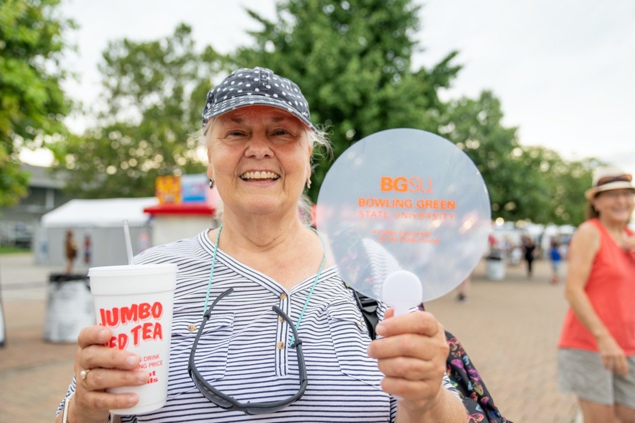 Woman wearing black polka dot ballcap holds a BGSU fan and jumbo iced tea cup at Ohio State Fair