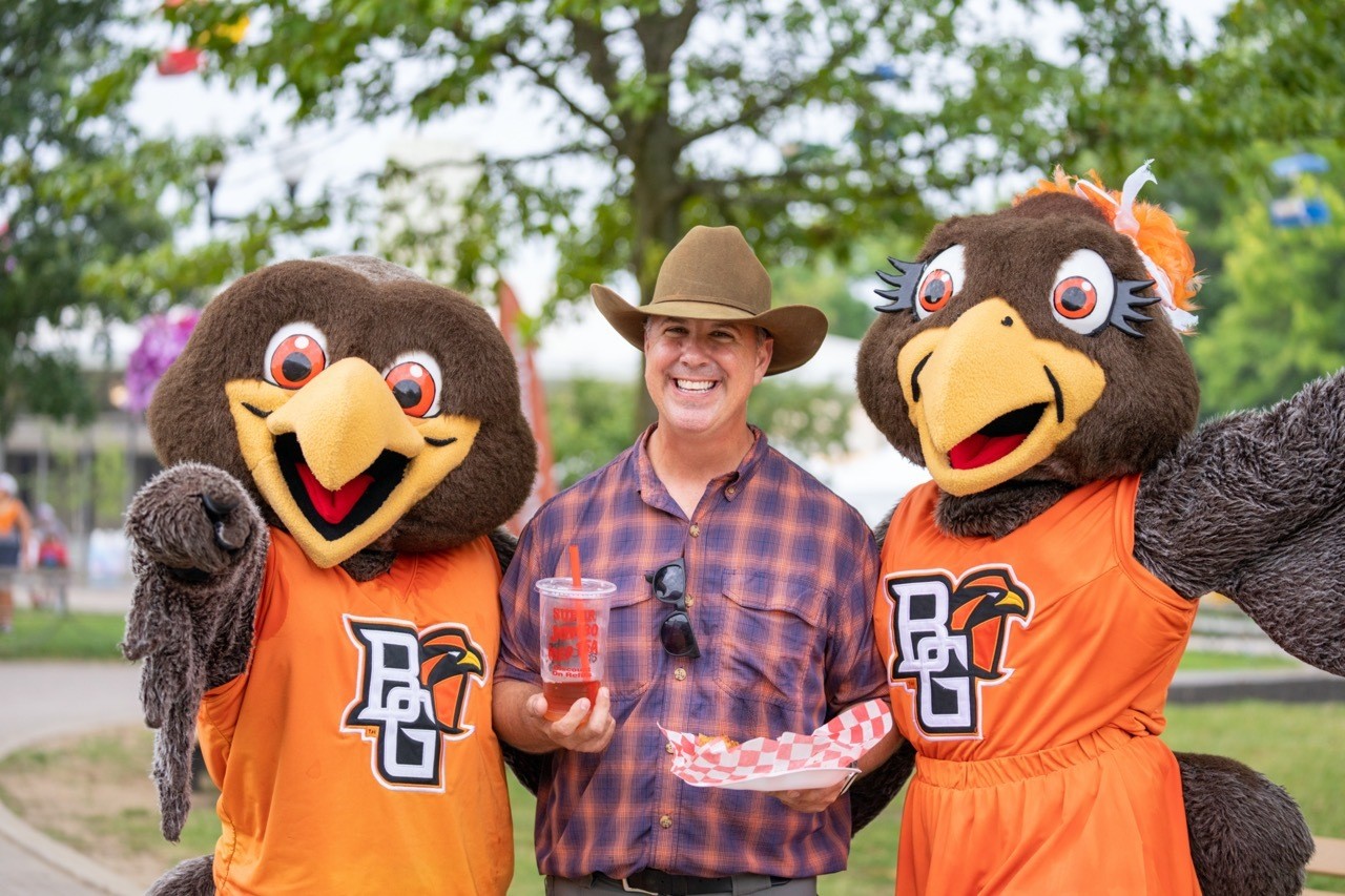 BGSU mascots Freddie and Frieda Falcon flank a man in a cowboy hat at the Ohio State Fair midway
