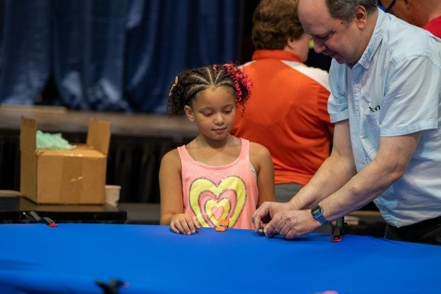 girl watches as older male prepares a ball bearing to spin down a large funnel-shaped experiment