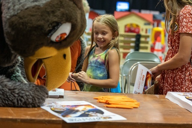 BGSU mascot Frieda Falcon signs a poster as a girl watches 