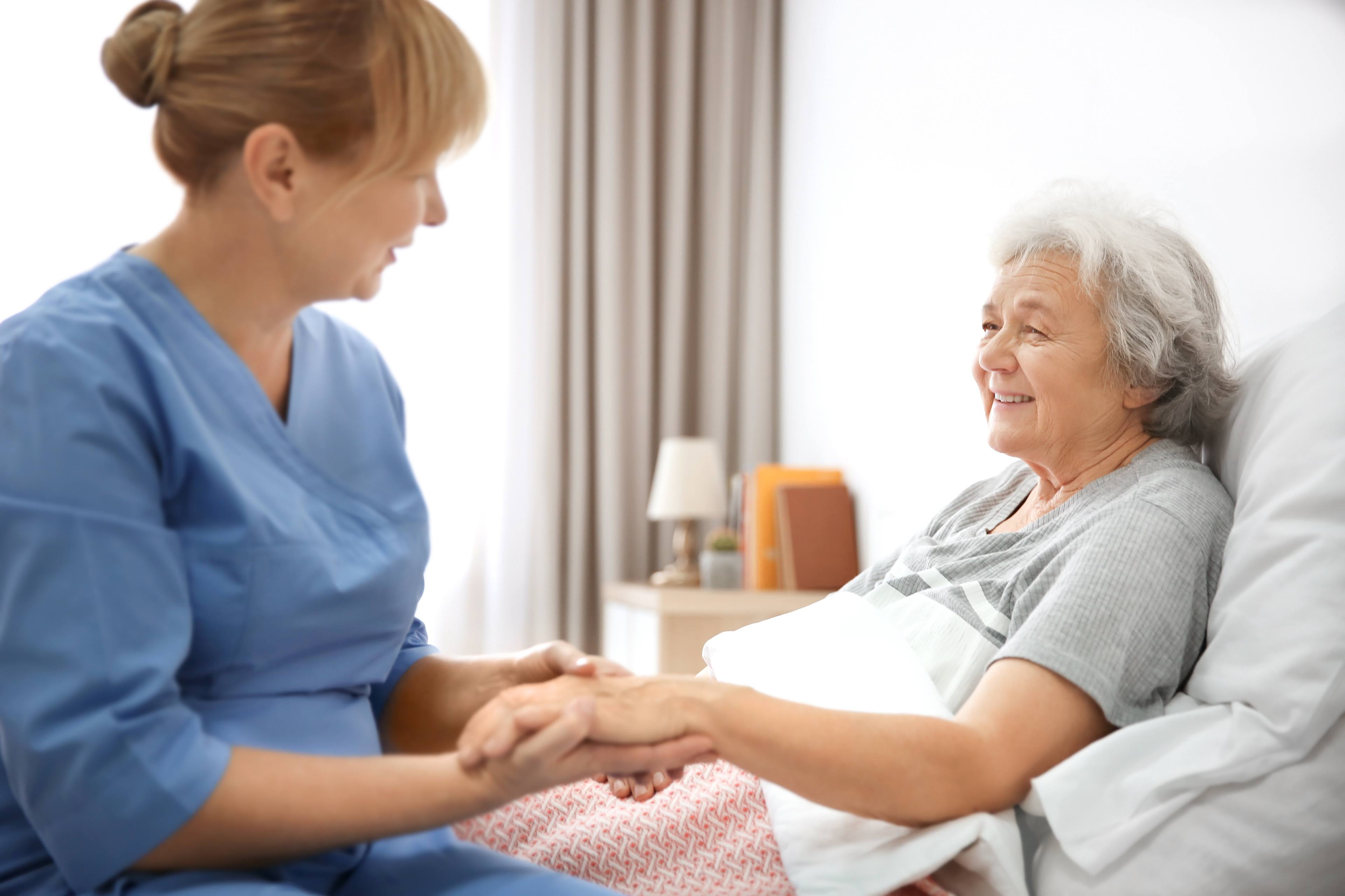 A female nurse holds the hand of a female patient.