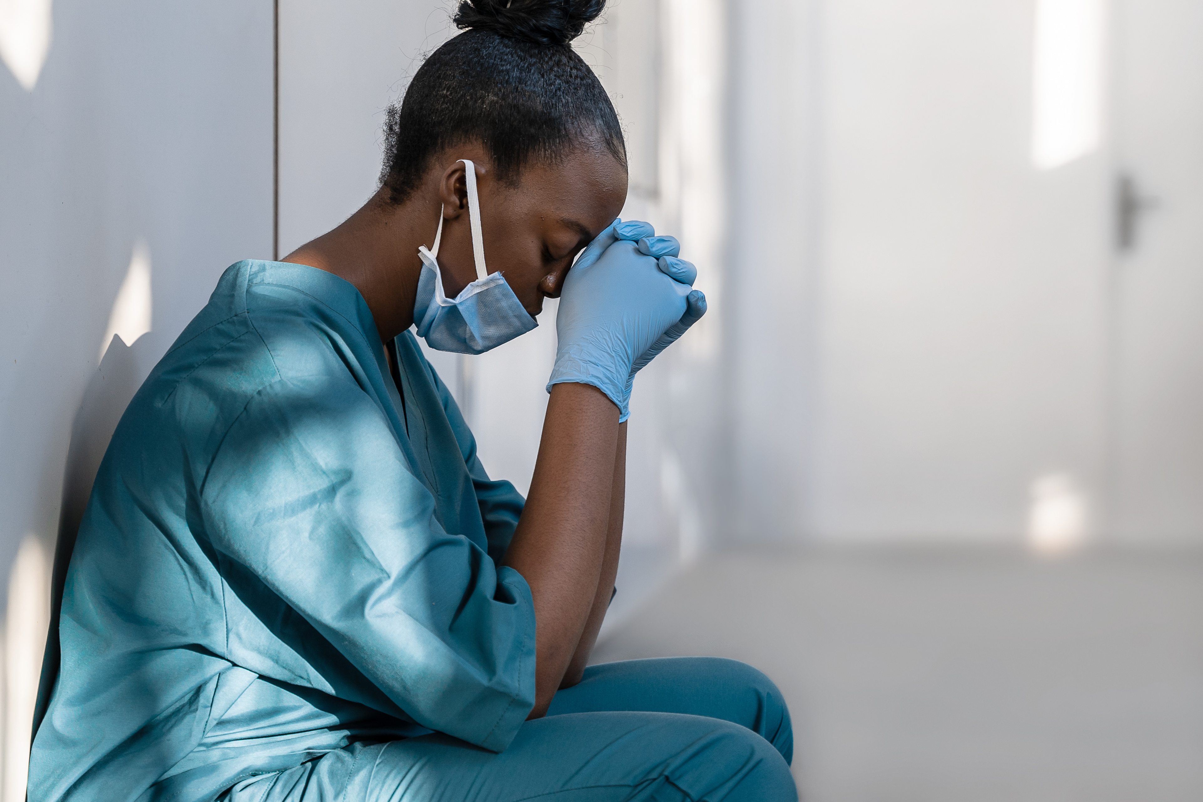 Nurse sitting in a hallway with her head in her hands.