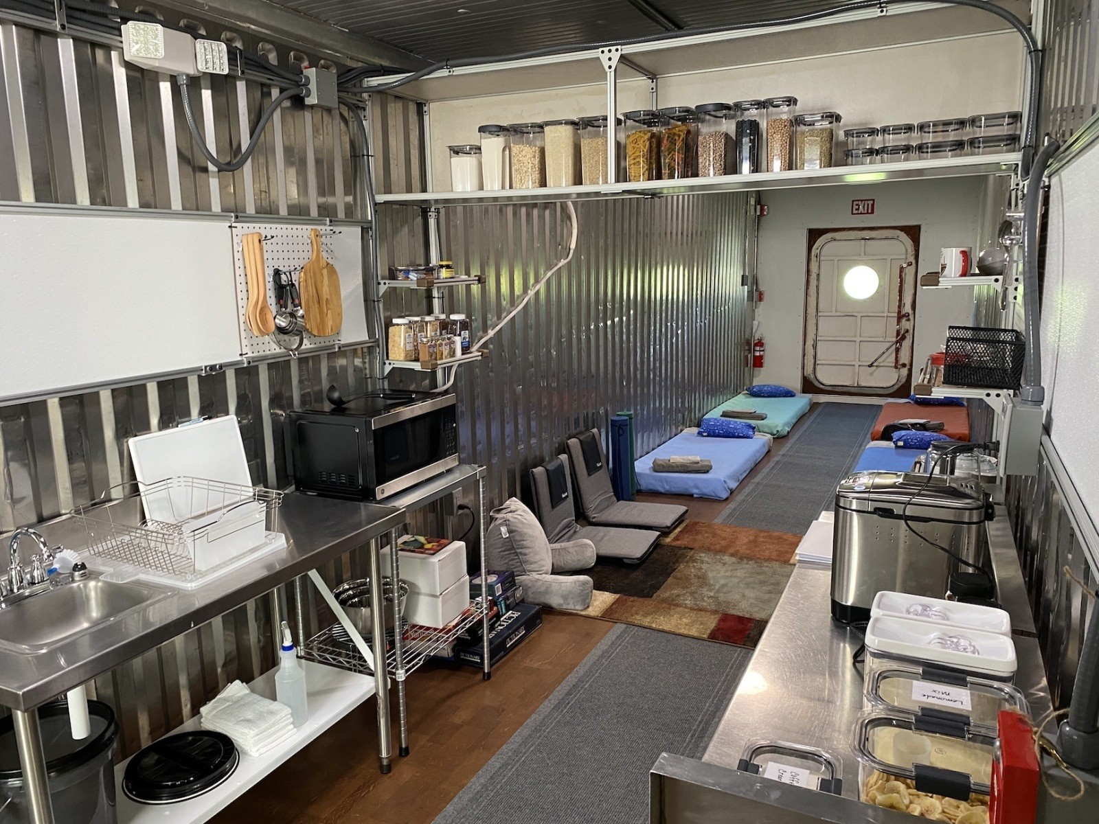 The common living area and kitchen in the Space Analog for the Moon and Mars. The photo is taken from the kitchen, looking out into the common living area. A couch, table, sink, microwave, and refrigerator are visible in the common living area.