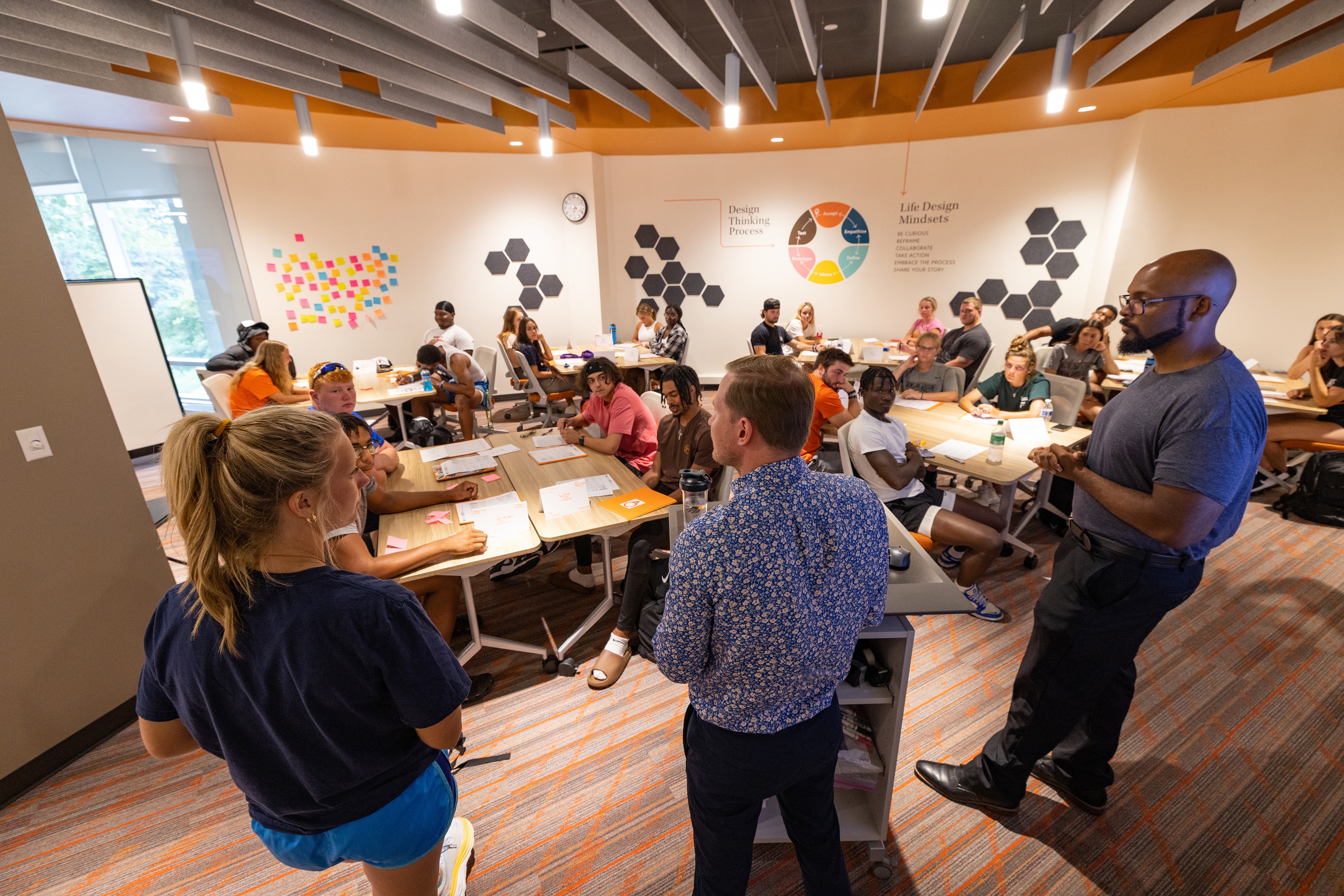 A group of people stand in a room to discuss Life Design concepts