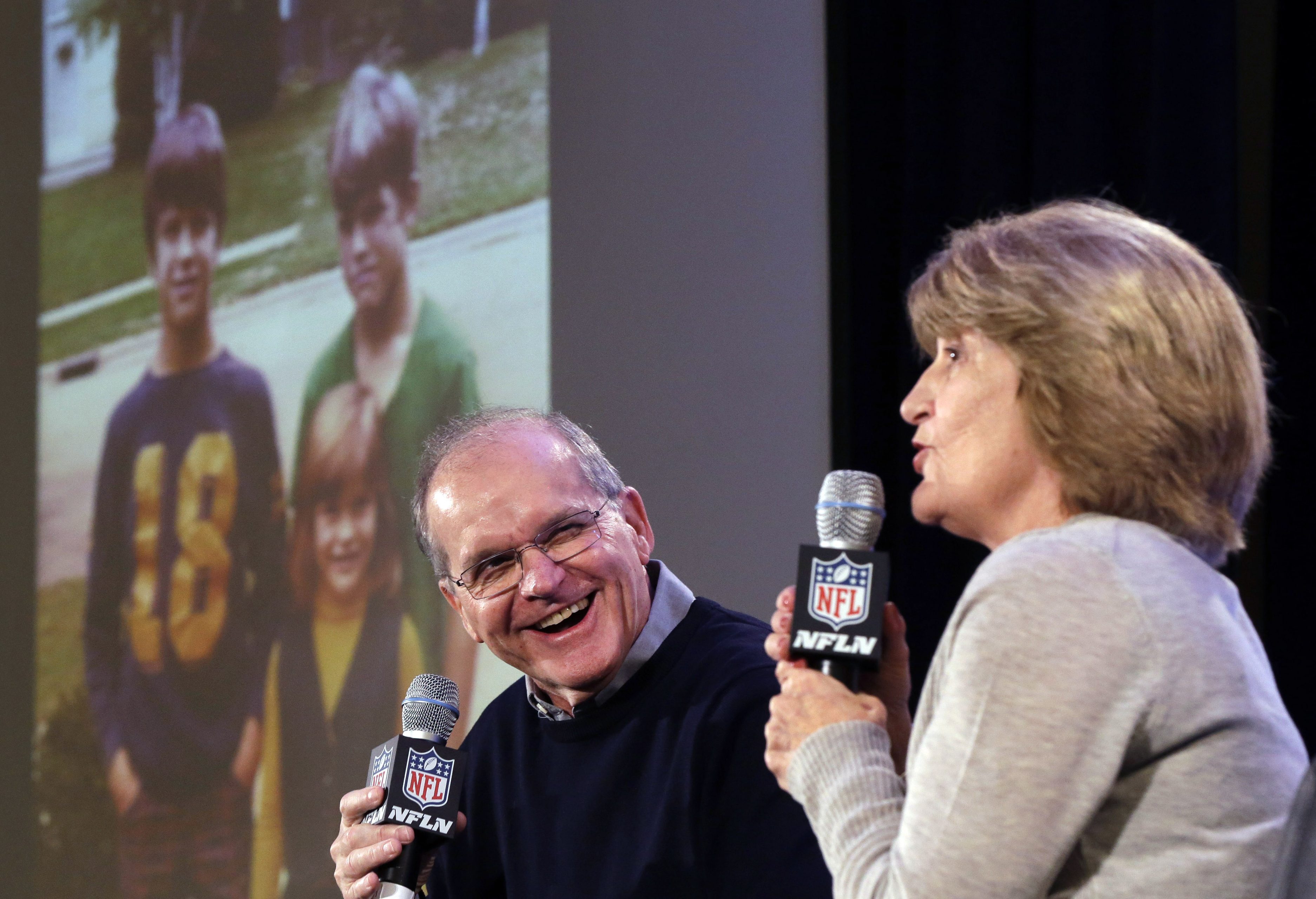 BGSU alumni Jack and Jackie Harbaugh speak into microphones while a screen projects a photo of their children, Jim, John and Joani Harbaugh.  