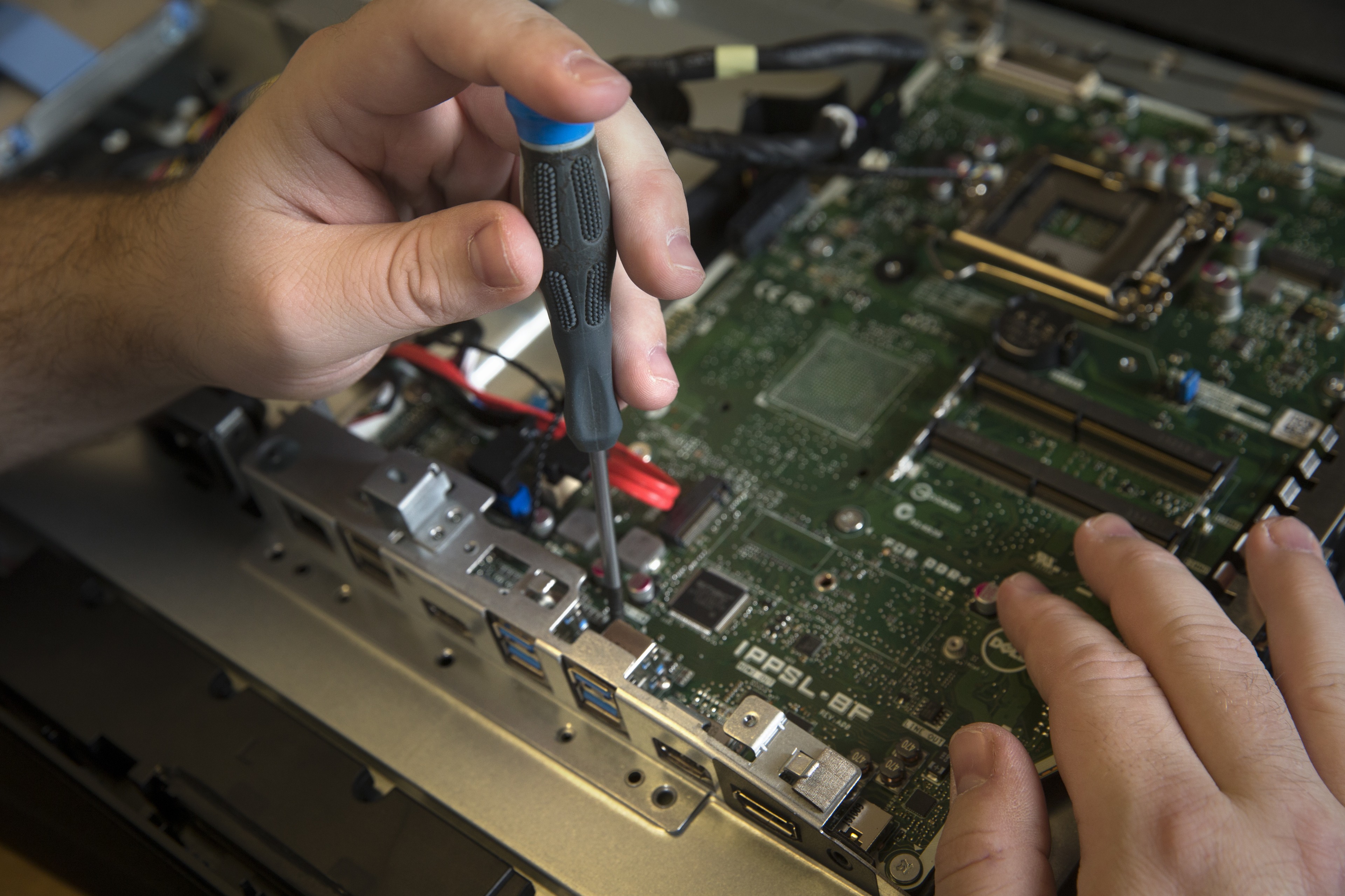 A hand holds a screwdriver to a circuit board