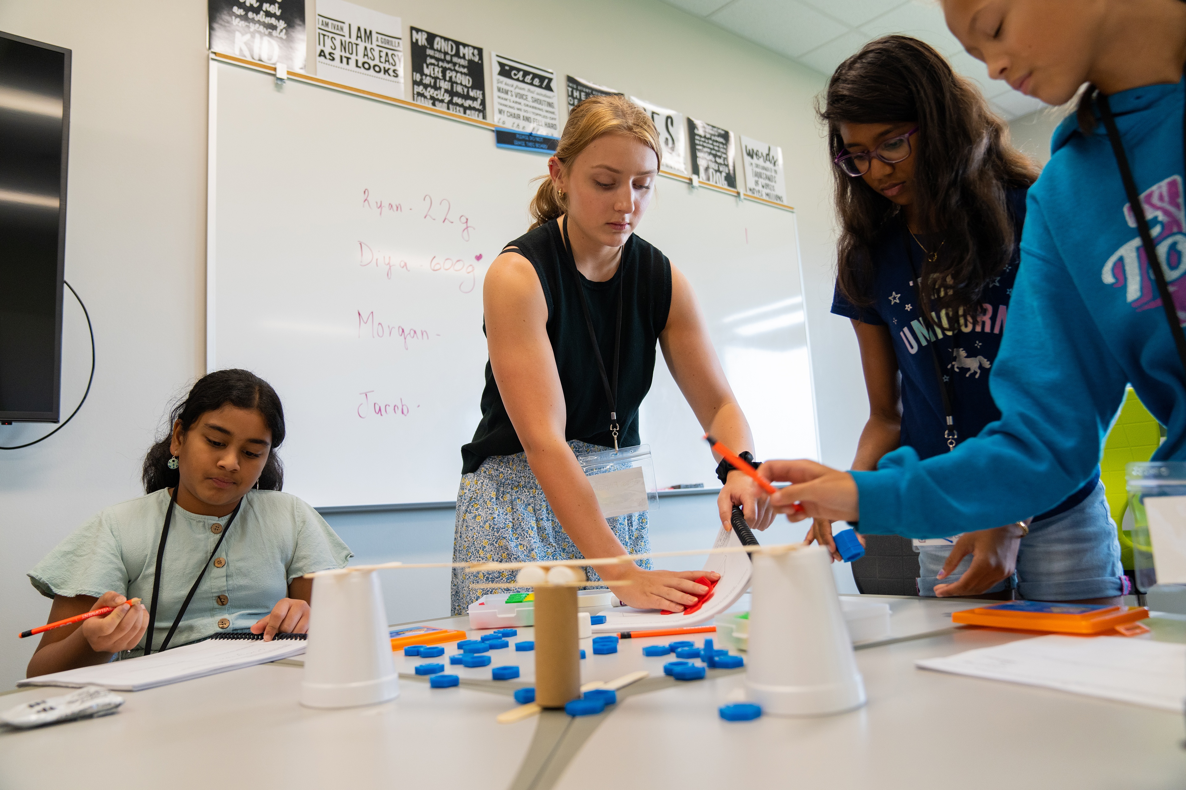 Tutor Jillian Filipiak aids students with an engineering project that uses a toilet paper tube and two styrofoam cups to make a bridge. 