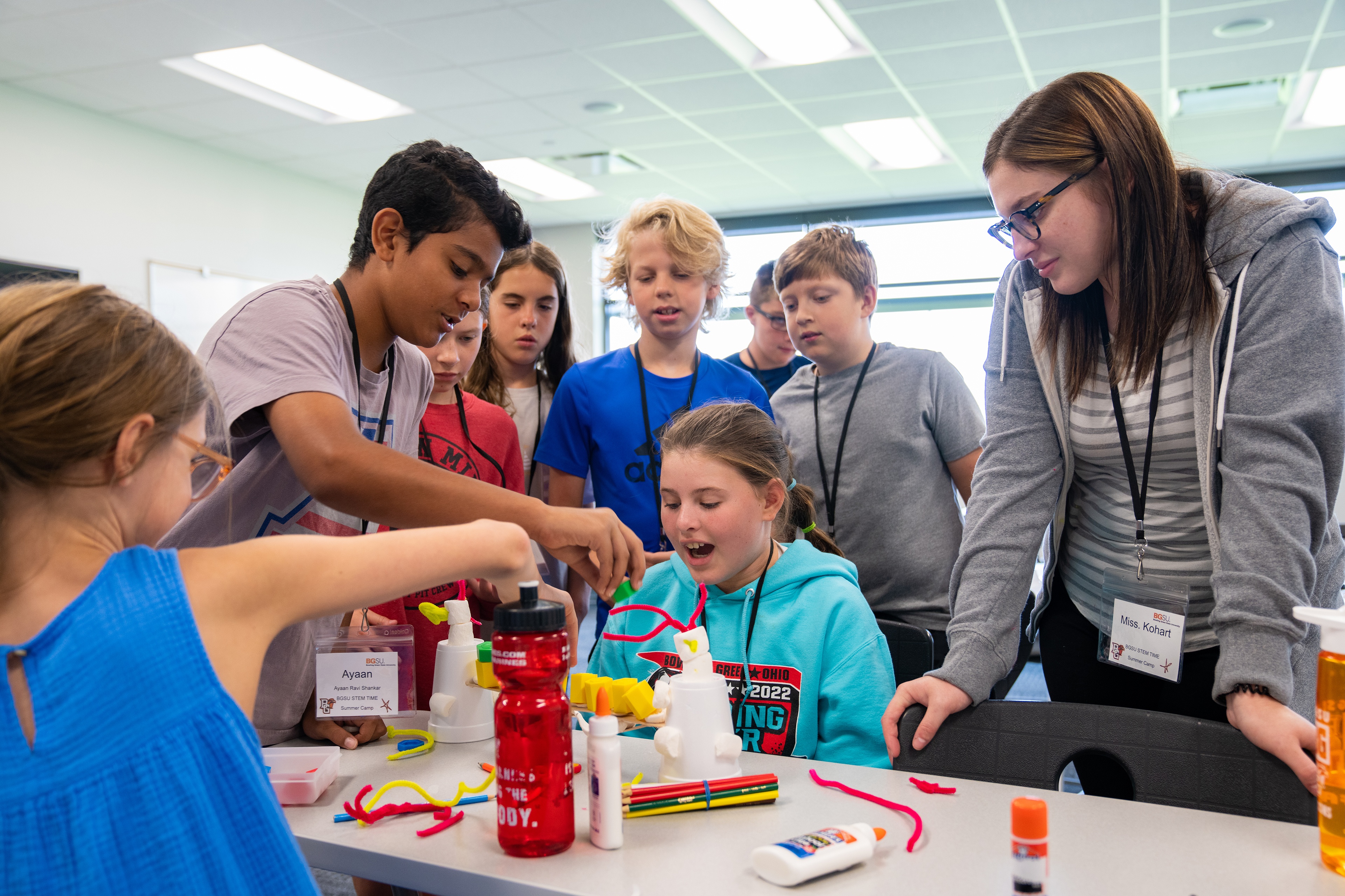 Students watch in a group as one student attempts to complete an engineering project with pipe cleaners.