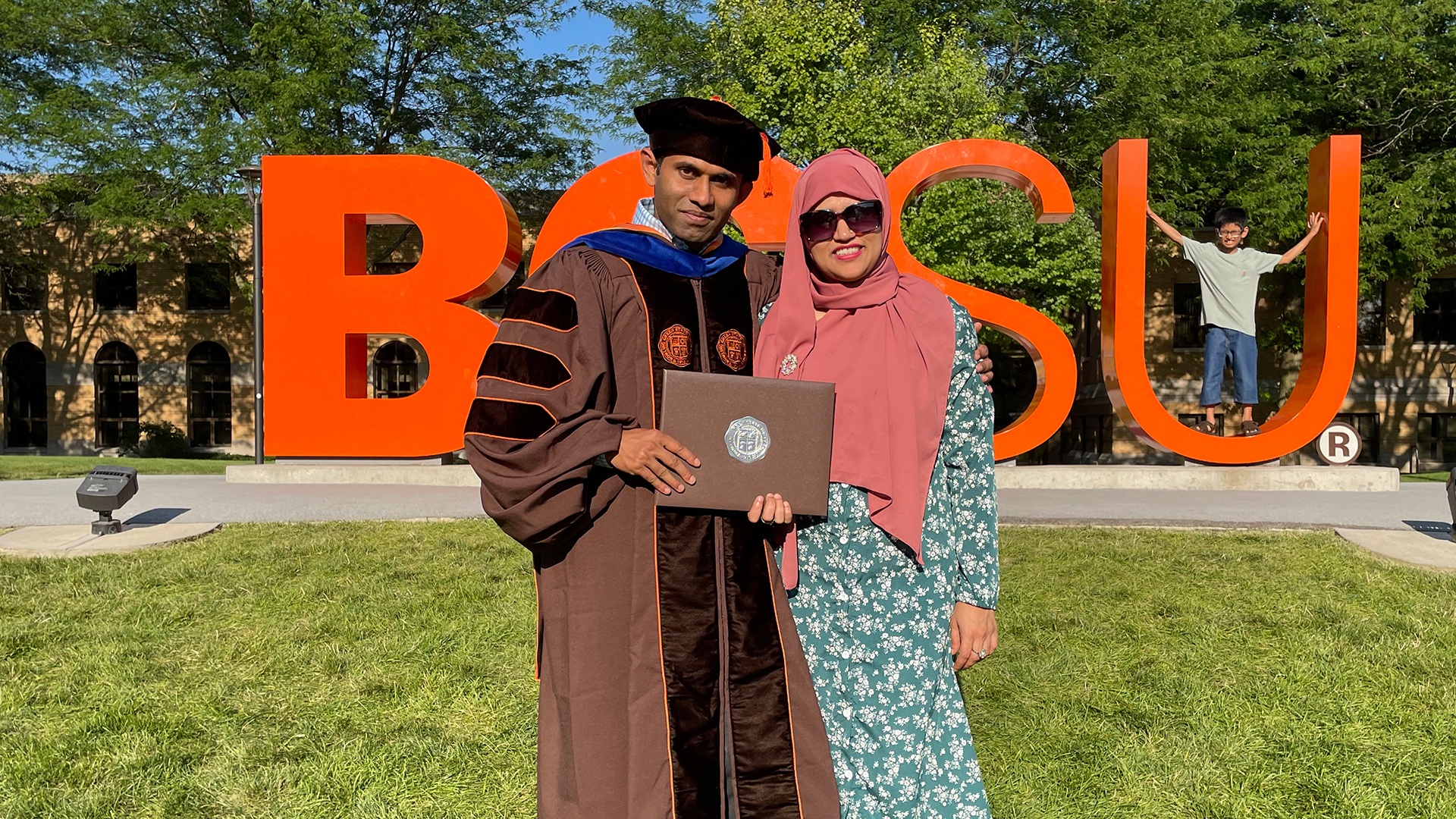 A man and woman standing in front of the BGSU letters and a child in the background.