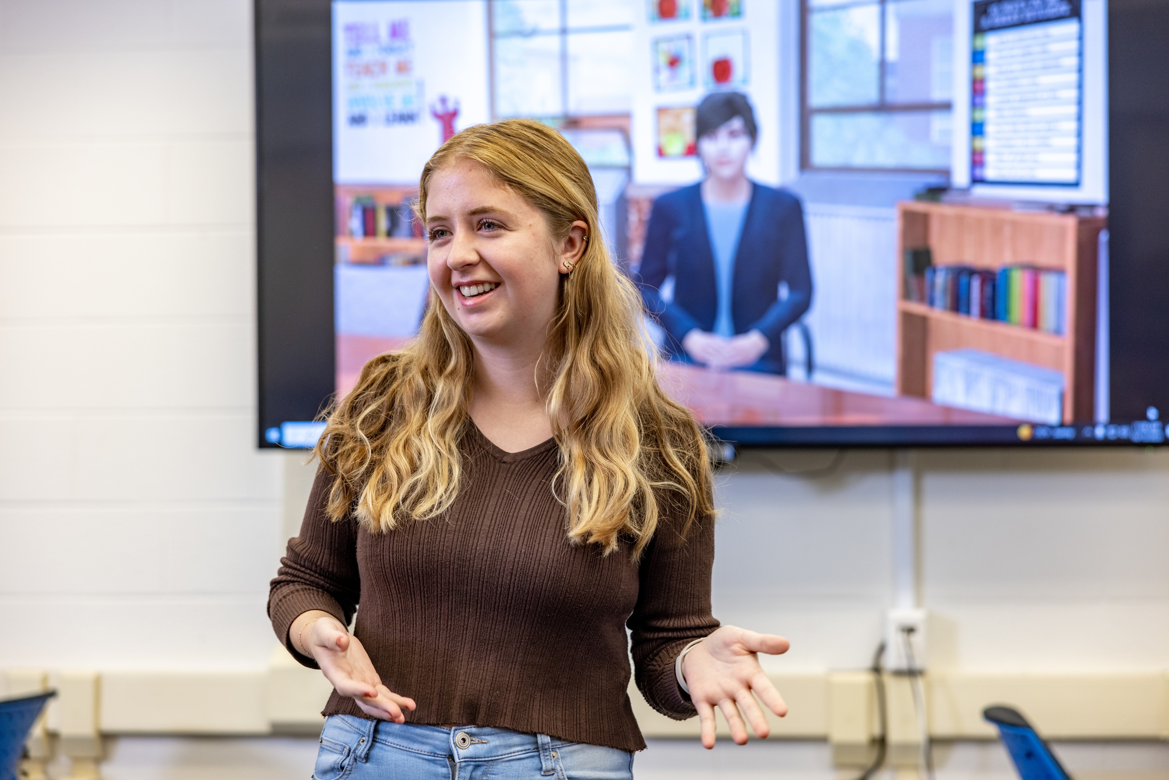 A BGSU student stands in front of a screen showing a simulated person in a Mursion display.