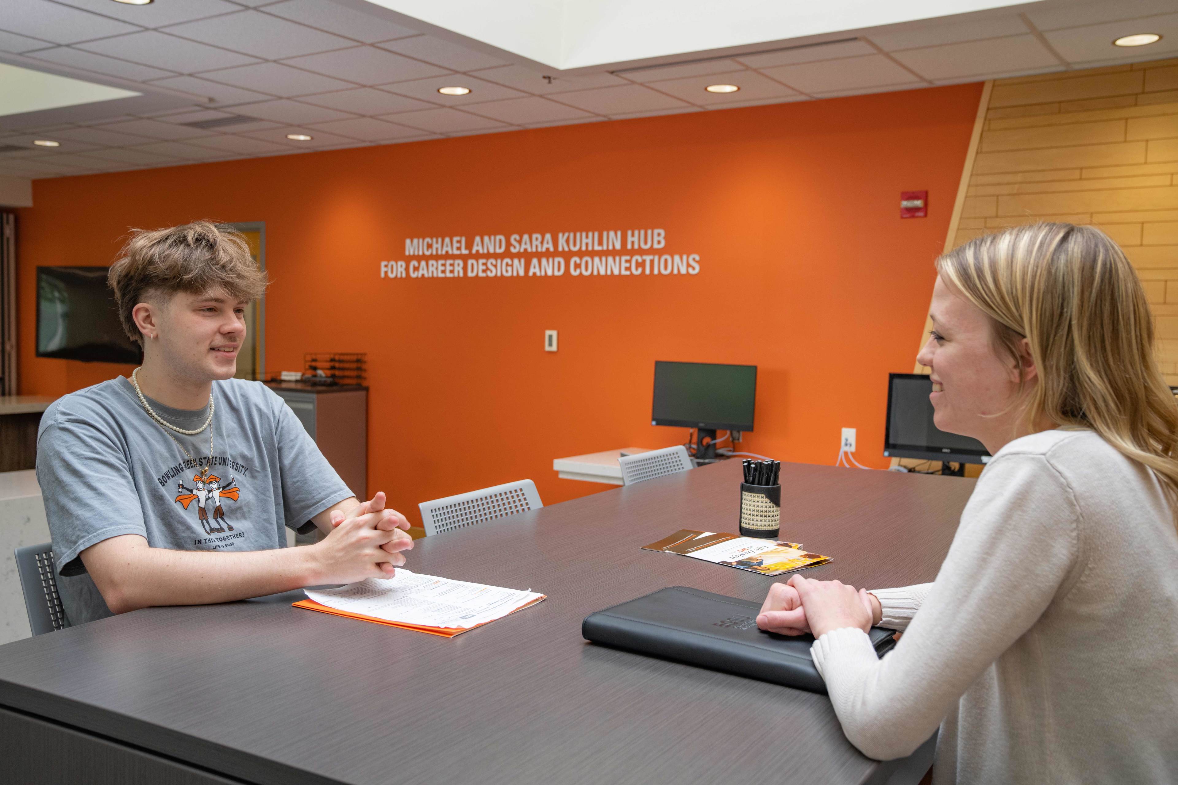 Two people sit at a desk.