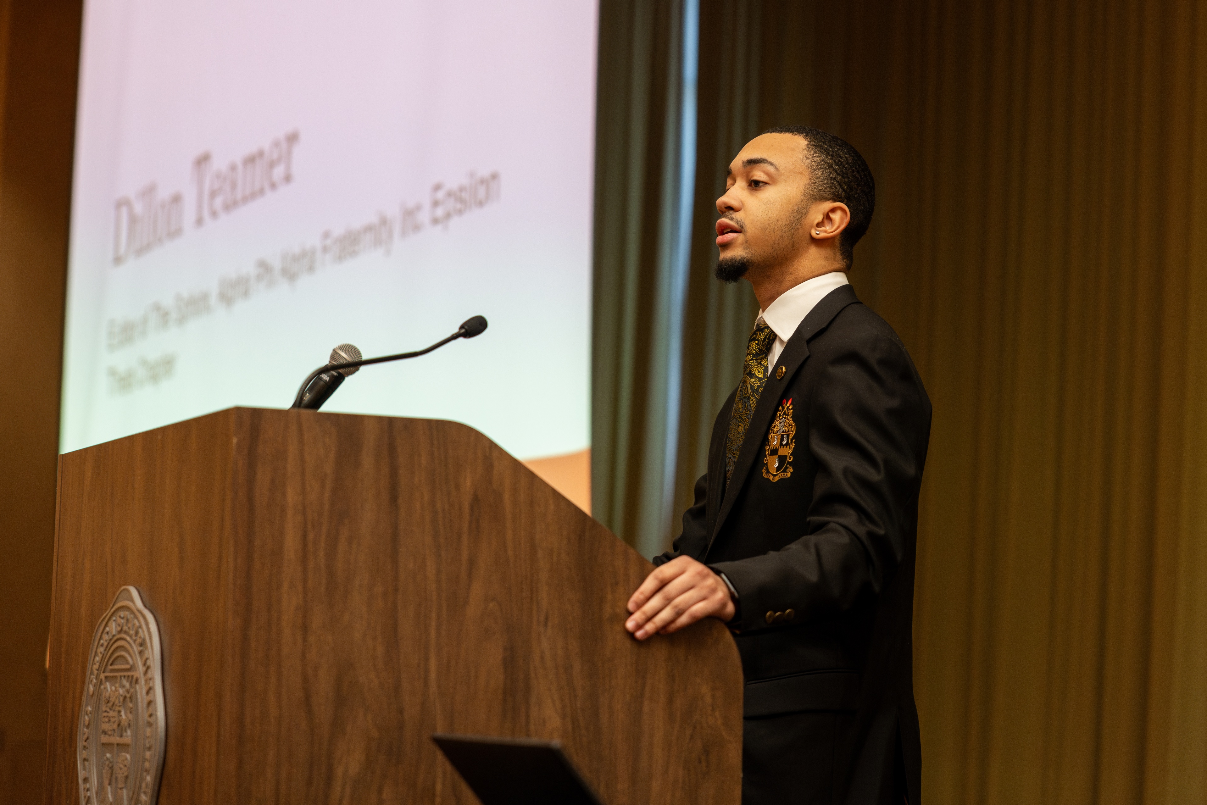 Dillon Teamer stands at a podium and speaks into a microphone.