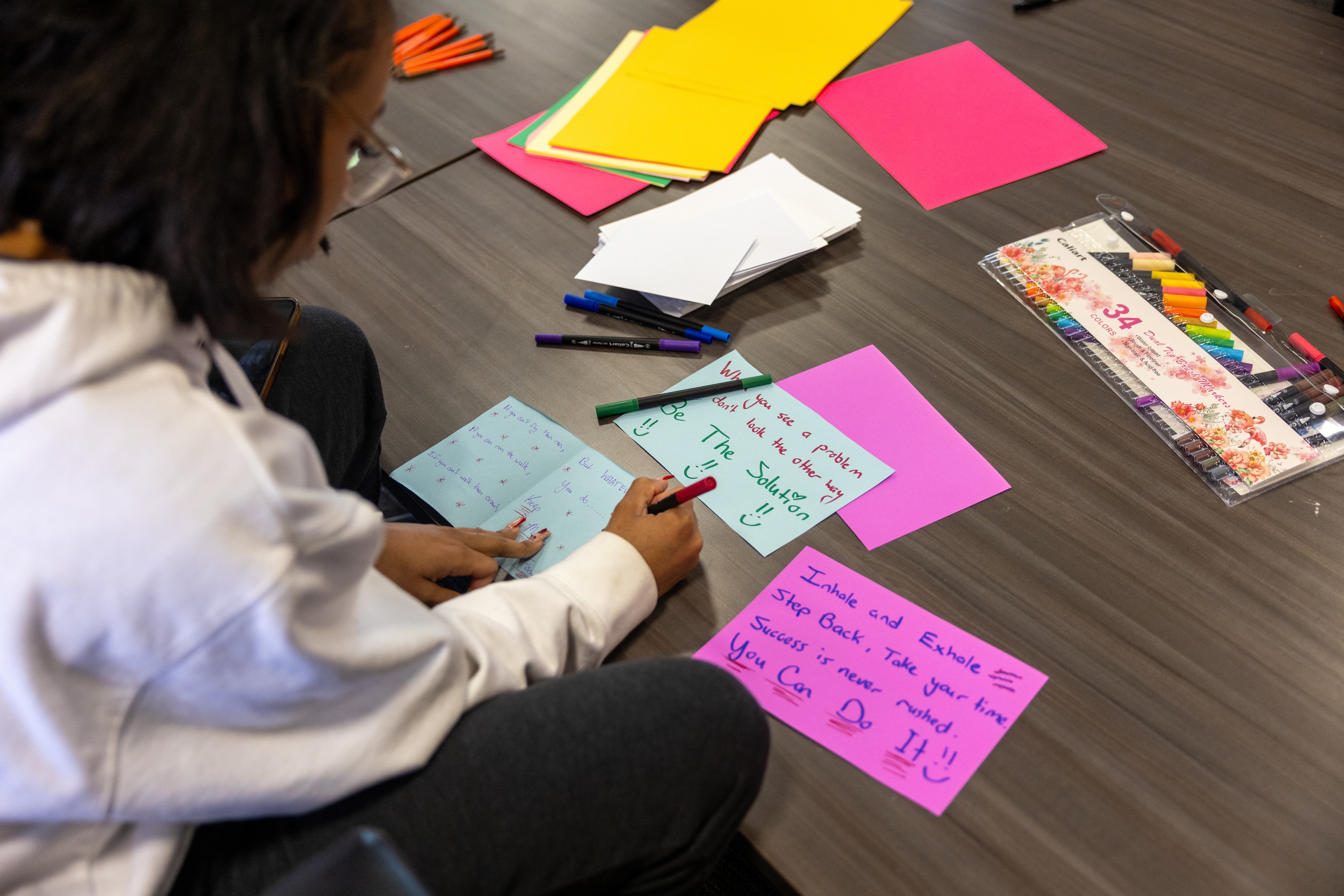A BGSU student using a marker and colored paper to create cards for others.