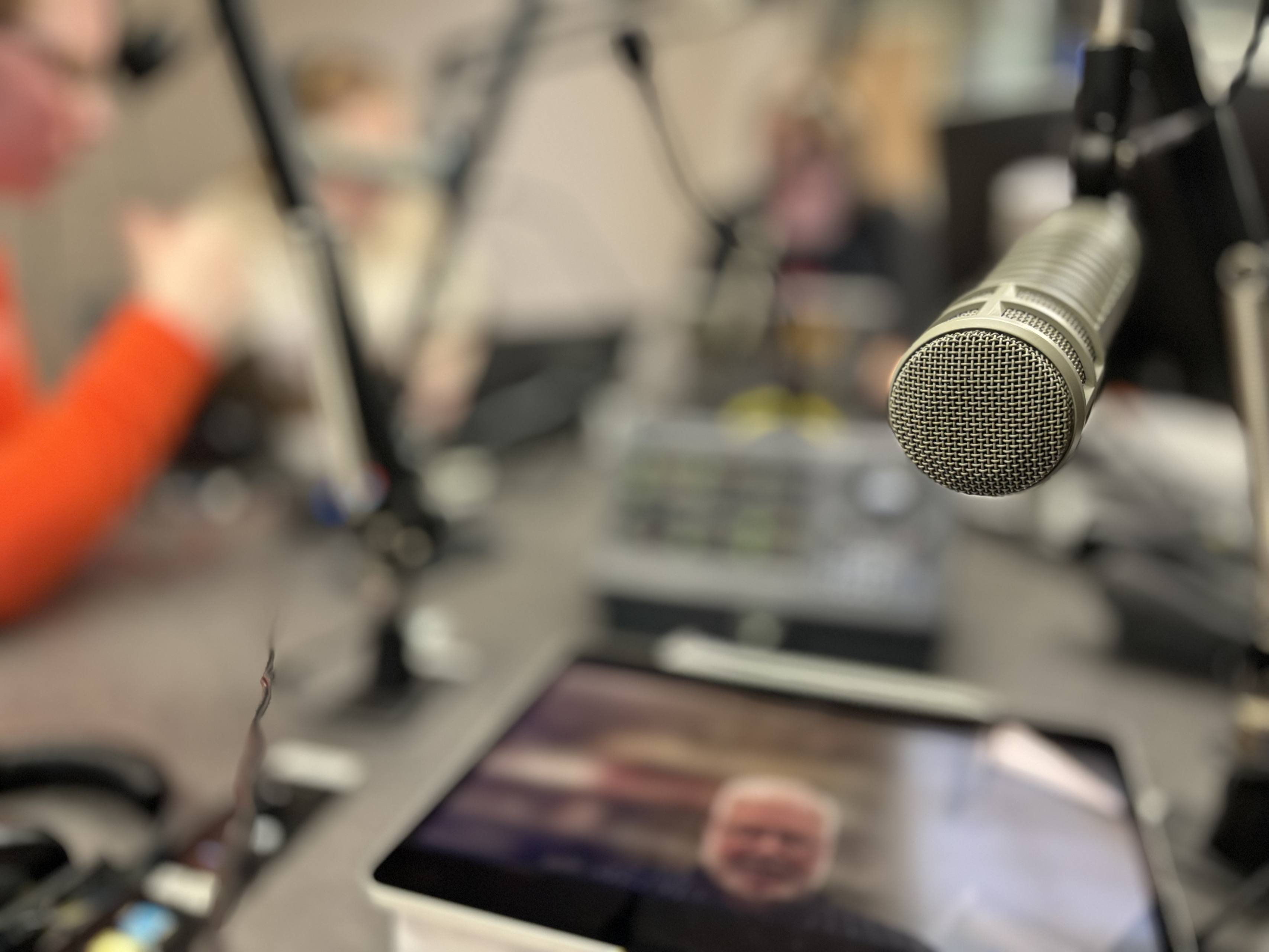 A microphone in the foreground with an out-of-focus iPad on a table. 