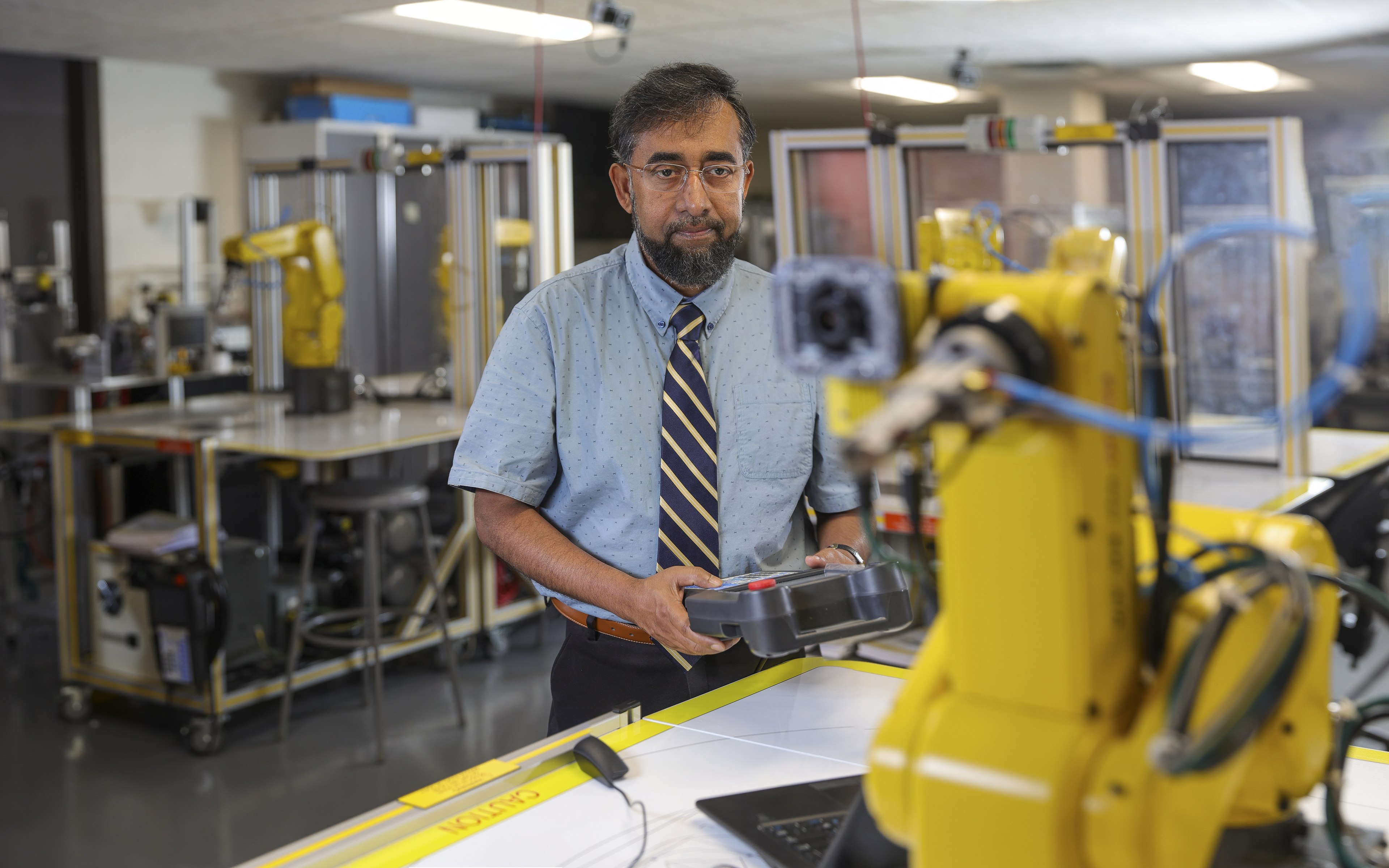 MD Sarder holds a large electronic device to control a Fanuc robot, which is in the foreground. 