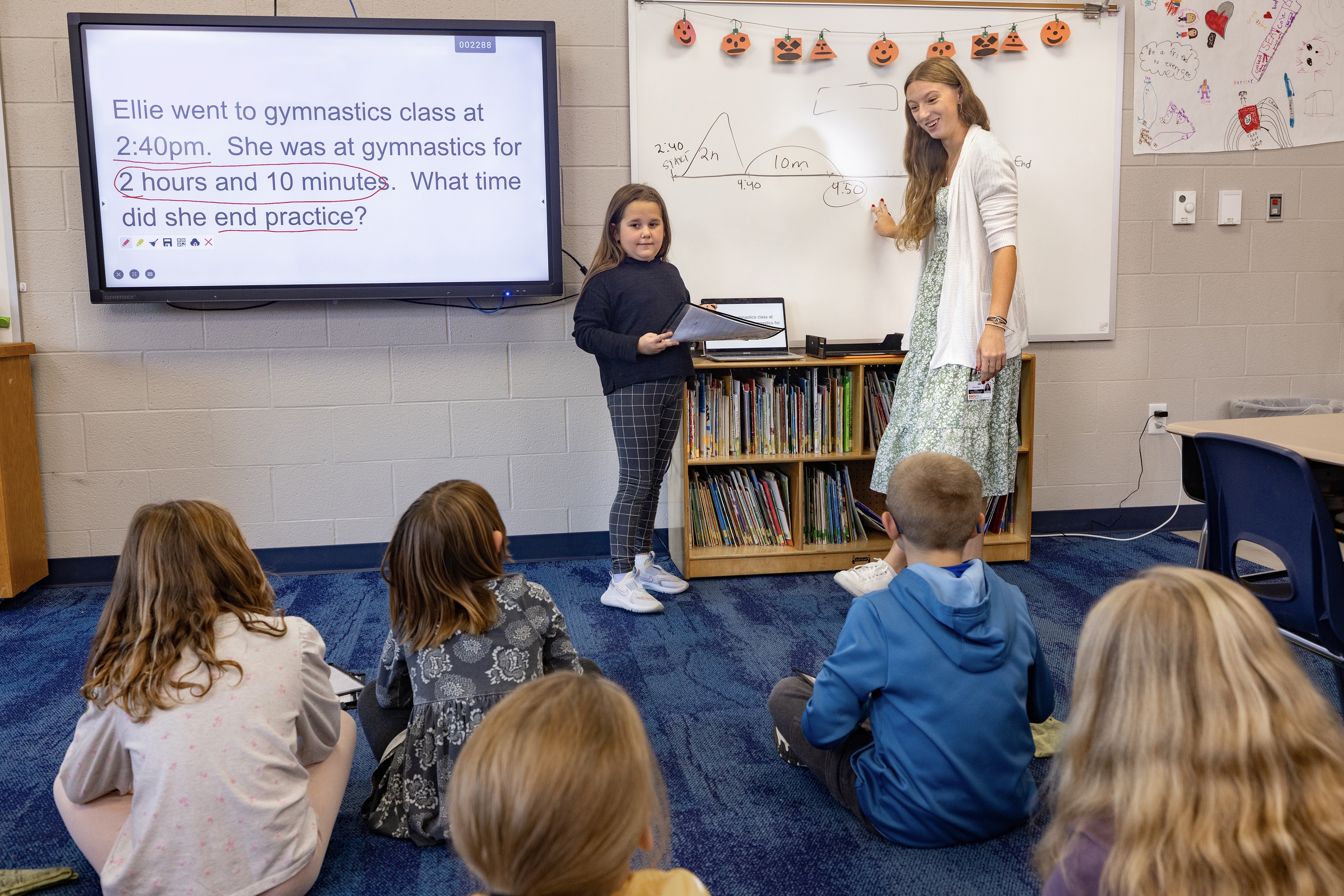 BGSU student Emma Haber points to a whiteboard while third-grade students look on. 