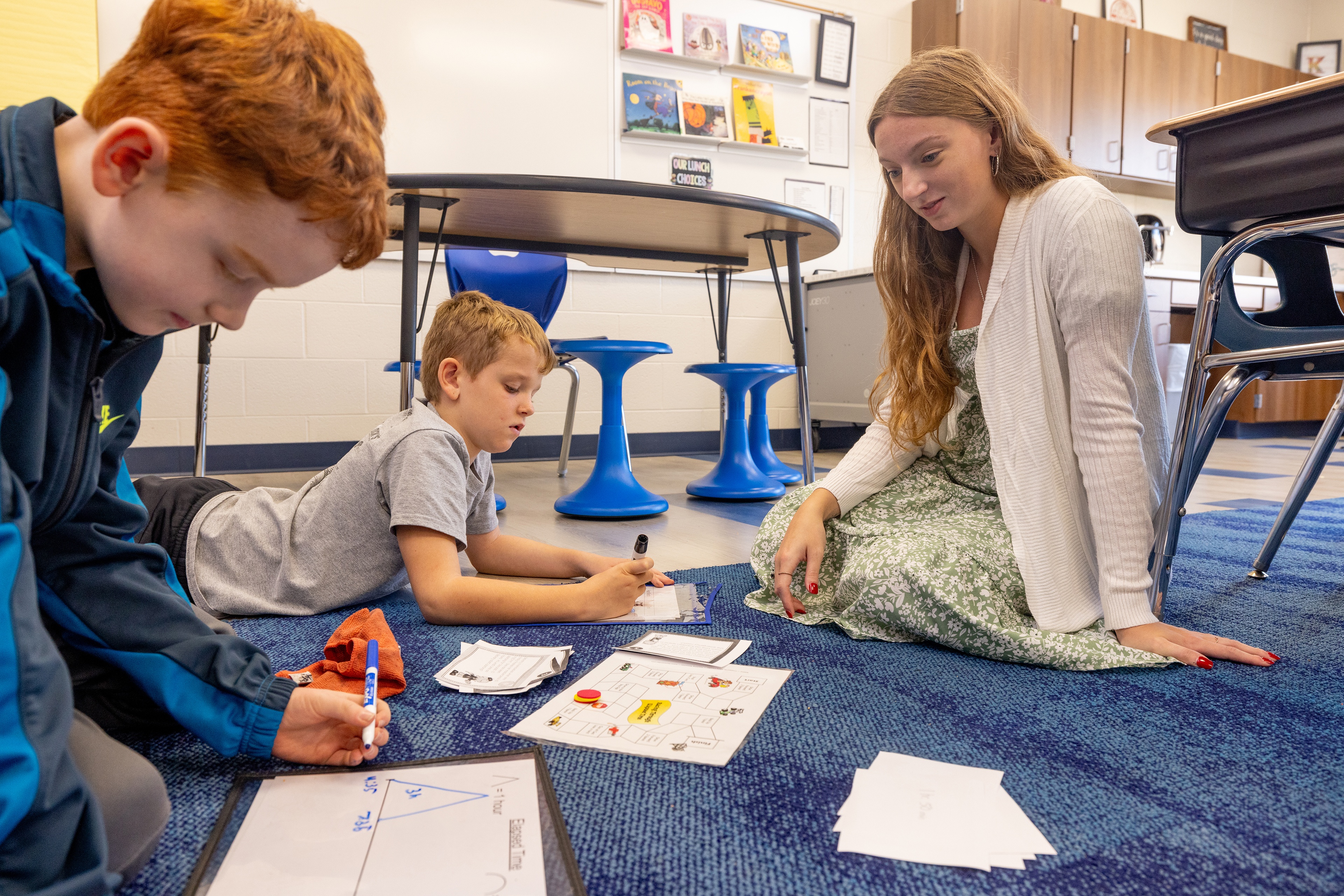 BGSU senior Emma Haber sits on the floor to help two students with their lesson.