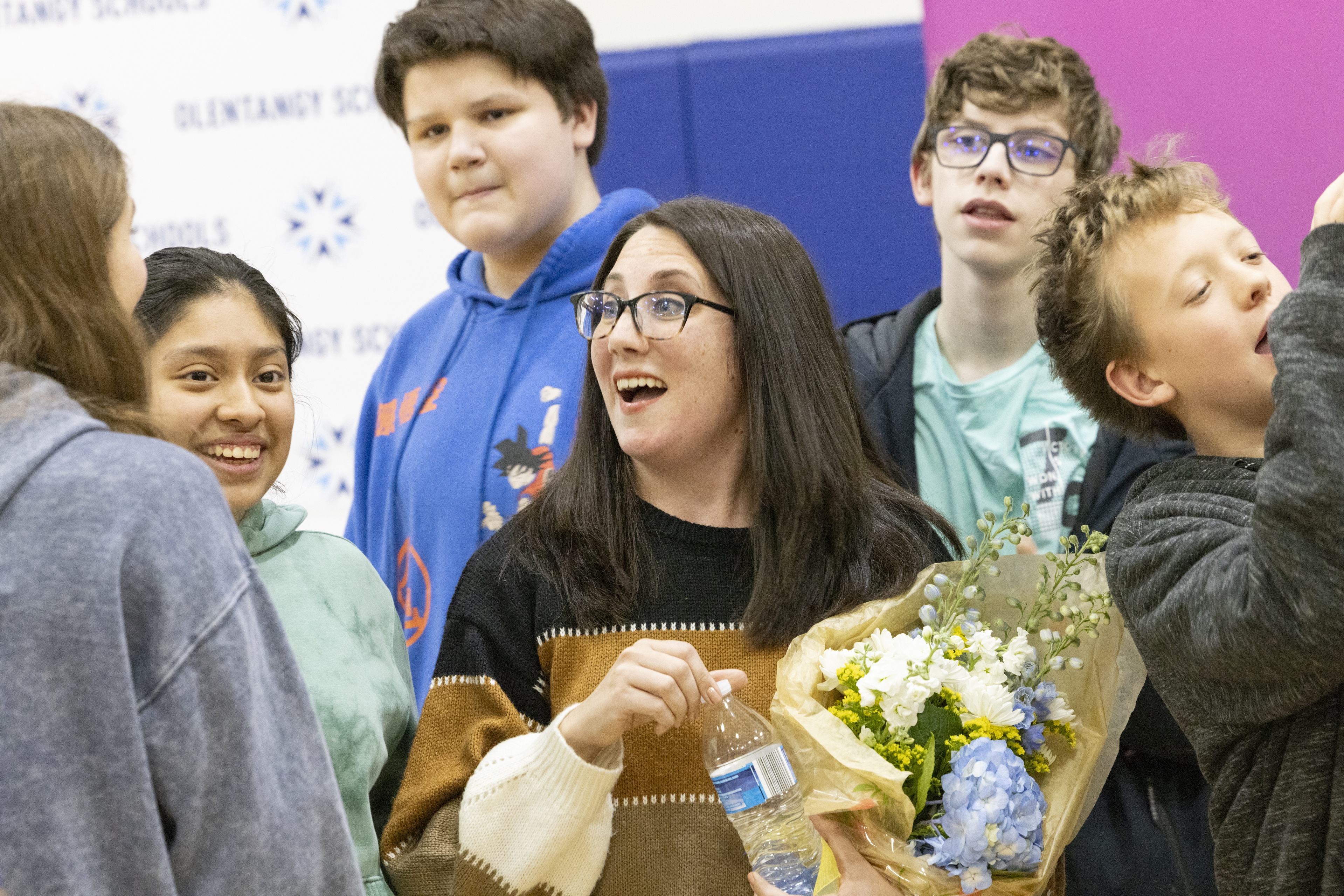 A woman holding a bouquet of flowers is surrounded by her students.