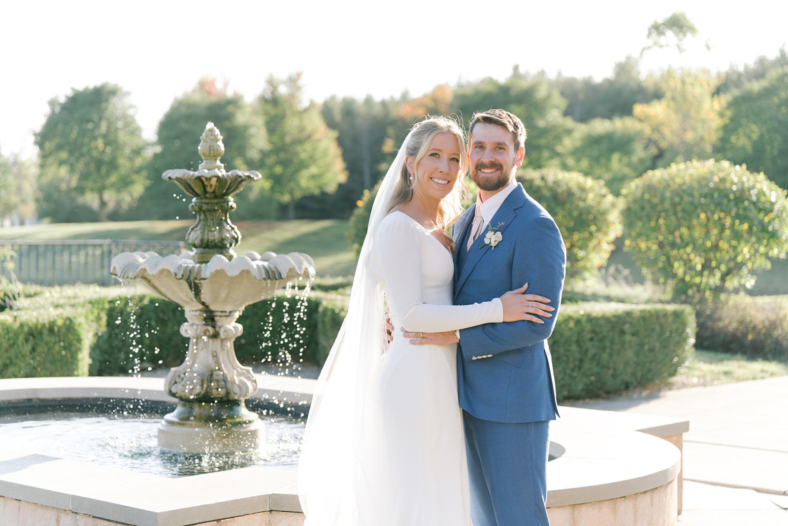 Bride Hailey Taberner and groom Kohl Taberner pose for a picture in front of a water fountain.