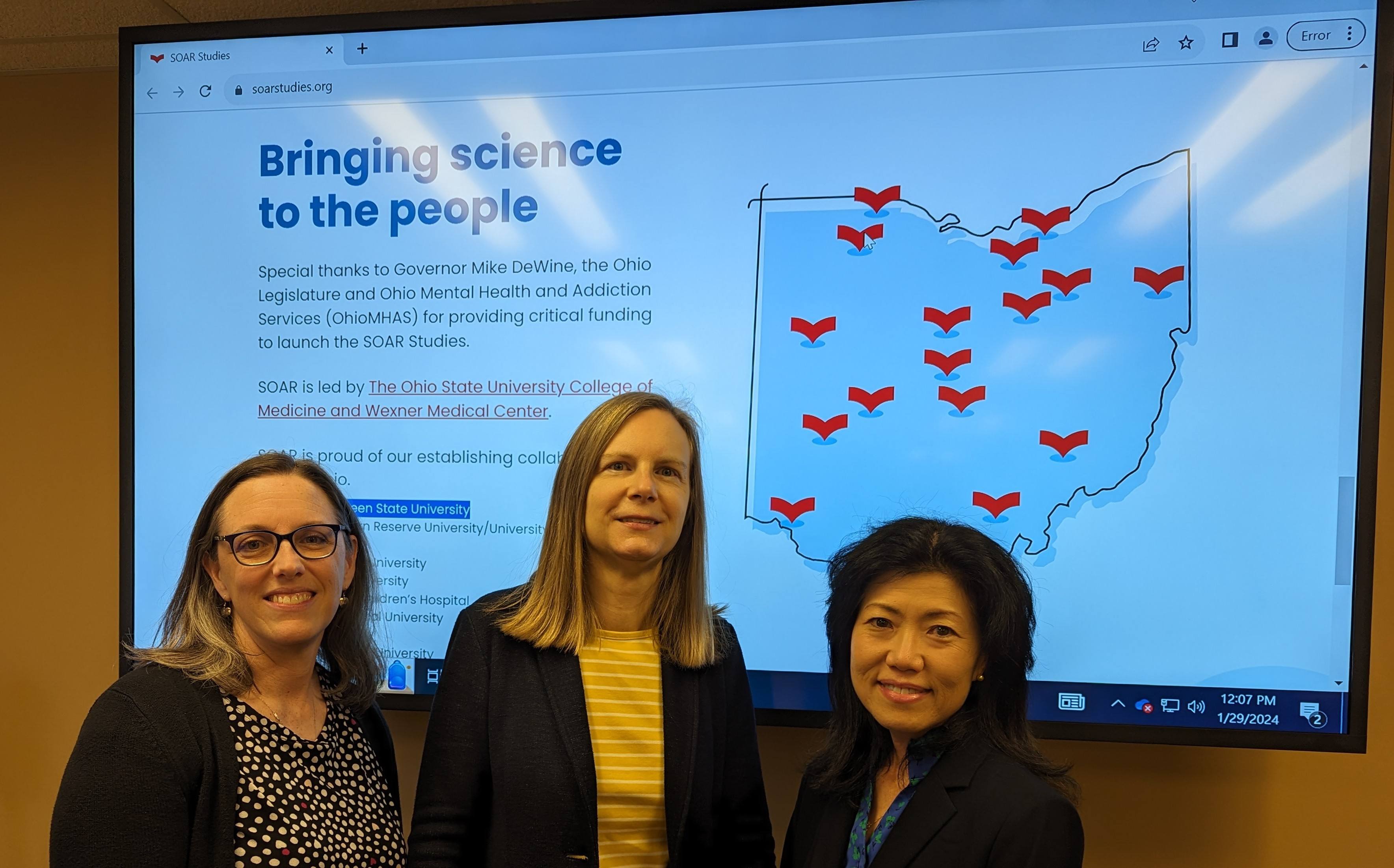 Three people stand in front of a presentation with the words, Bringing science to the people.