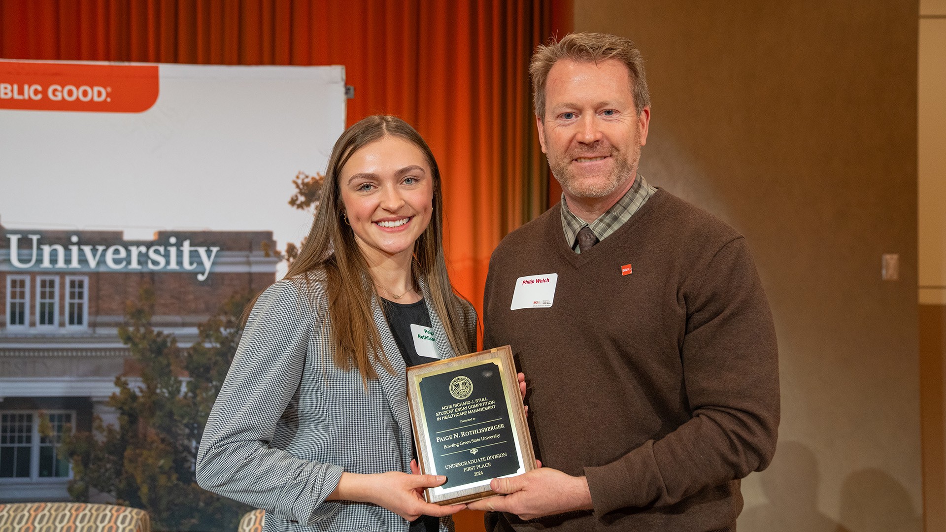 A woman and a man stand on stage holding an award plaque