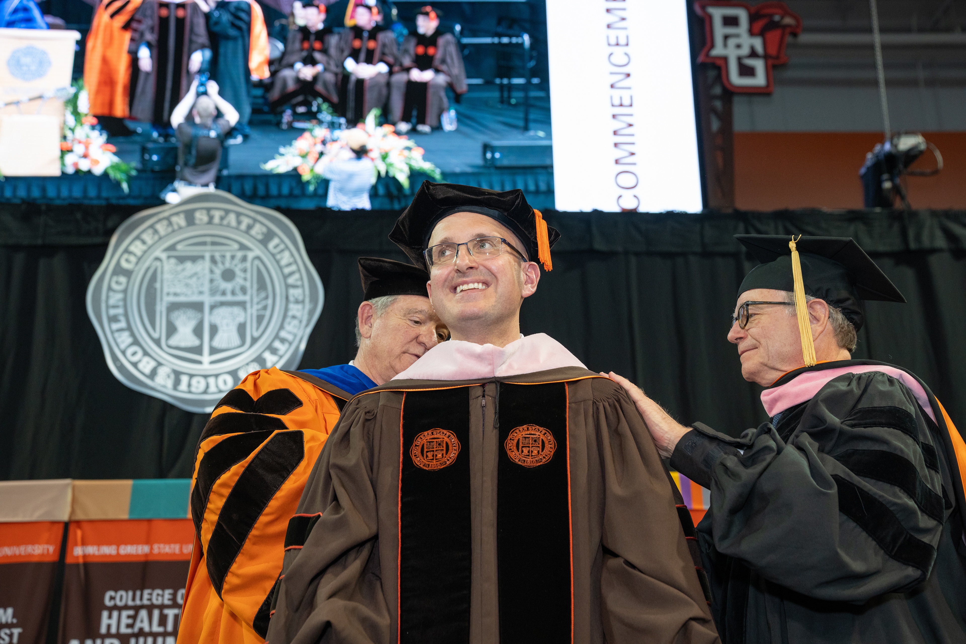 A man receives graduation regalia hood from BGSU President Rodney K. Rogers and Dr. Bruce Moss.