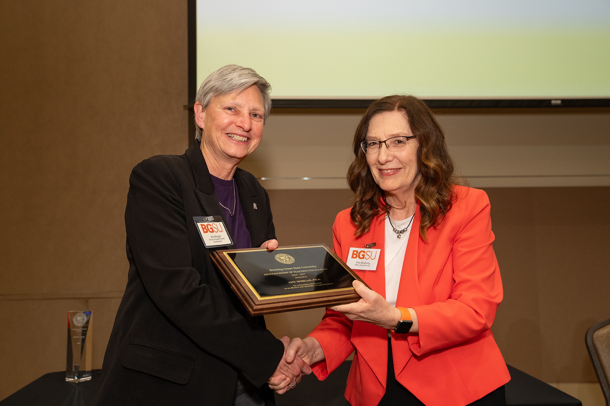 Two women hold a plaque and shake hands