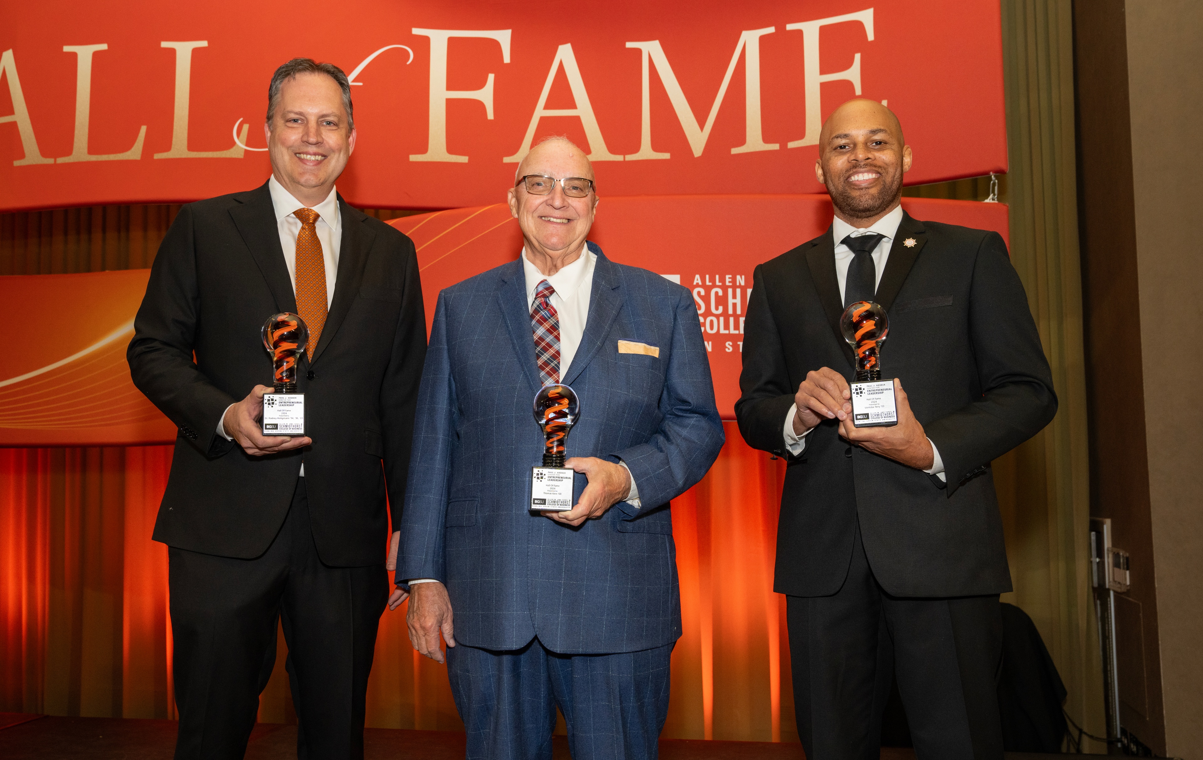 Three men pose for a photo with awards.