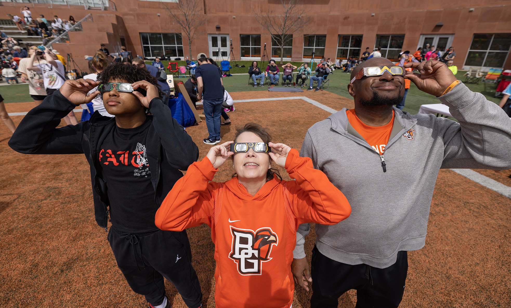 People wearing eclipse glasses sit on a football field