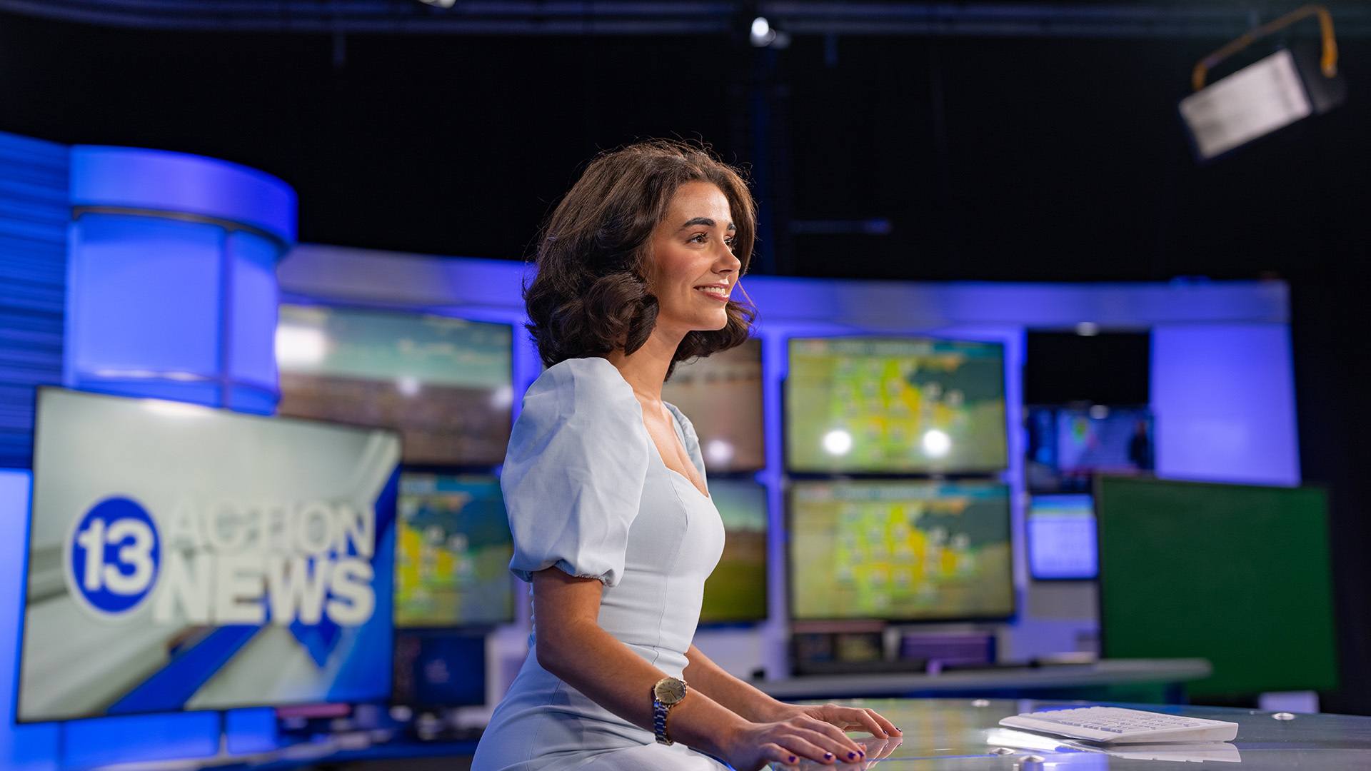 A person sits at an anchor desk at a television station.