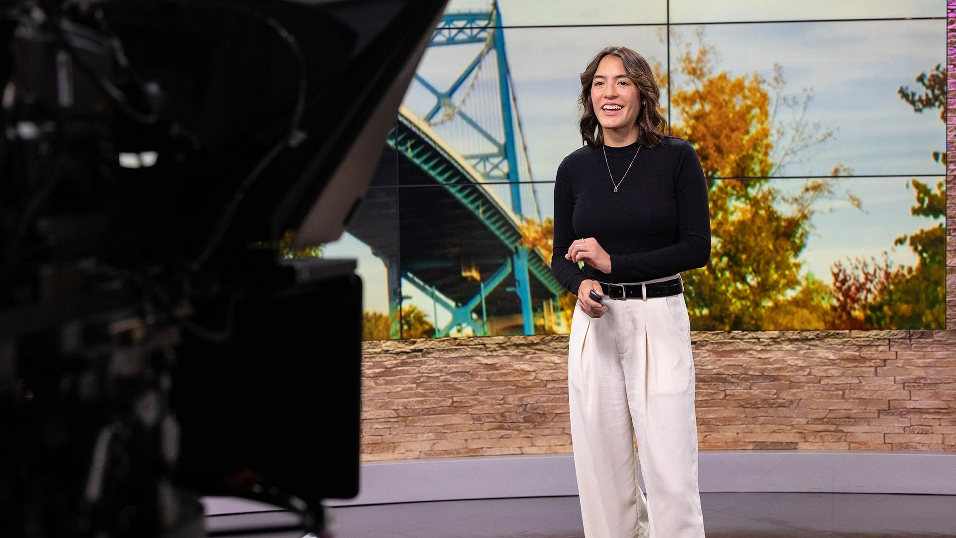 A person standing in front of a screen while reporting for a television station.