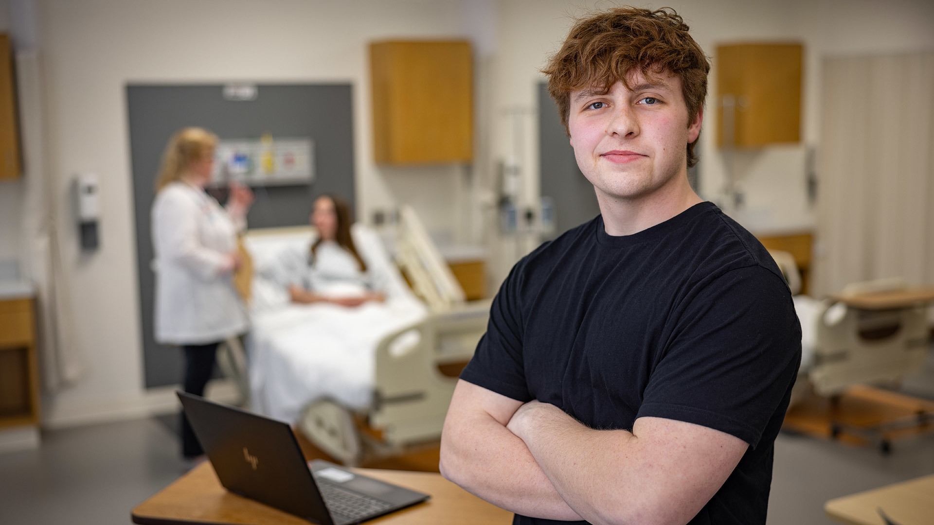 A person standing in a hospital room and a patient in the background.