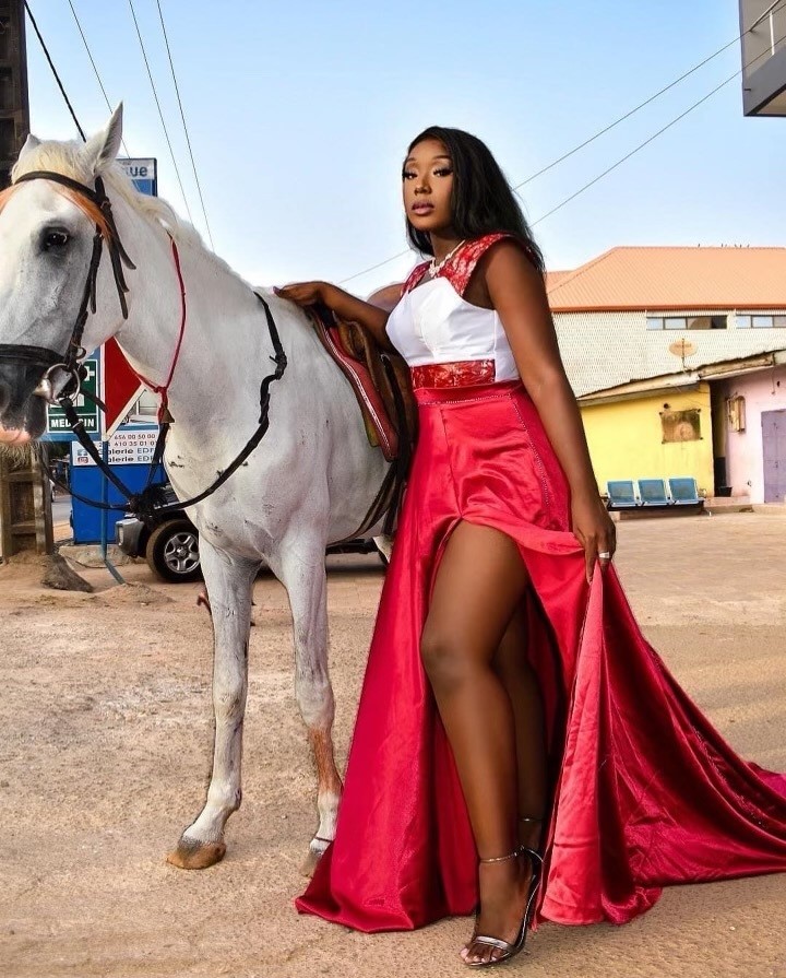 A person wearing a red and white dress while standing next to a white horse.